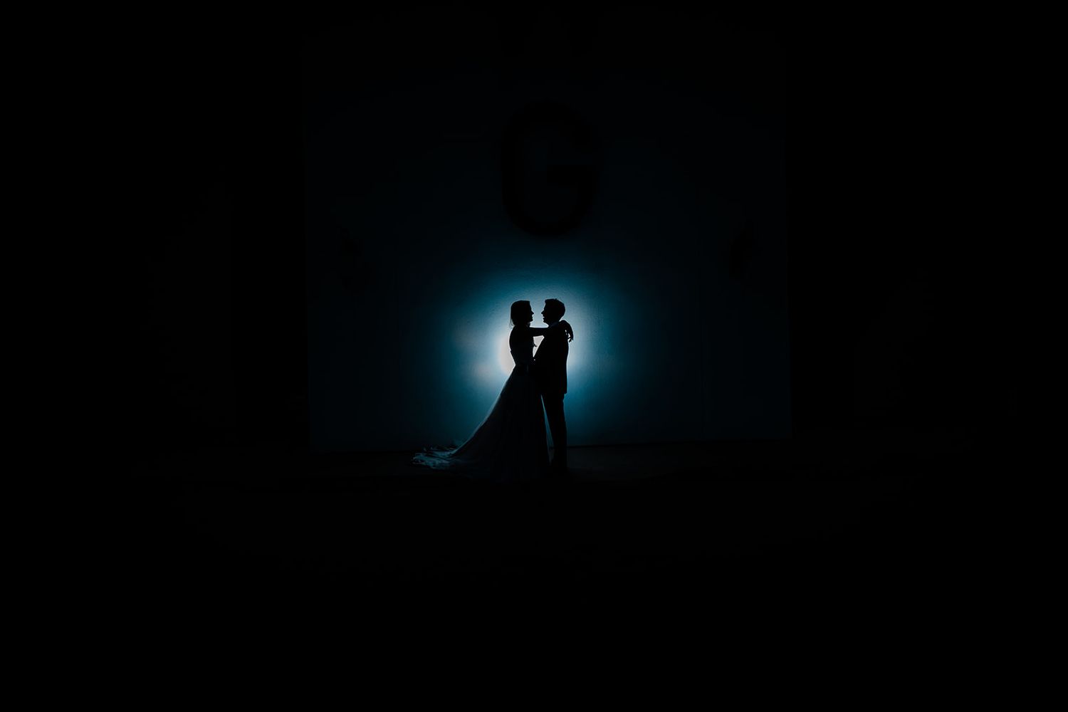 A romantic silhouette of a couple backlit by a glowing blue moon creates a dramatic wedding photograph.