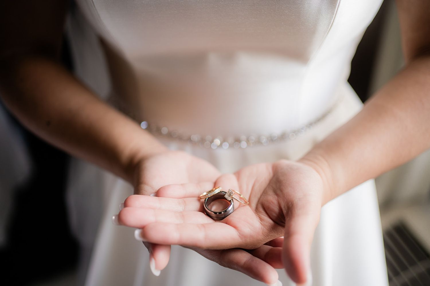 Close up view of hands holding a small dark wedding ring against white fabric.
