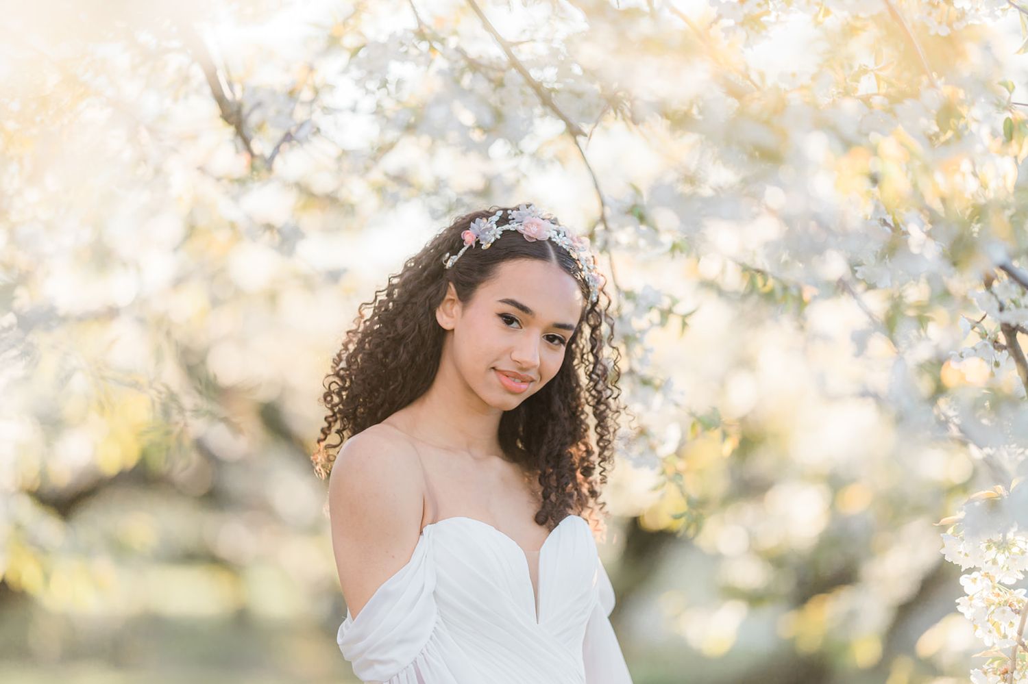 A dreamy spring portrait in white lace with blooming cherry blossoms in the background creating a soft, ethereal mood.
