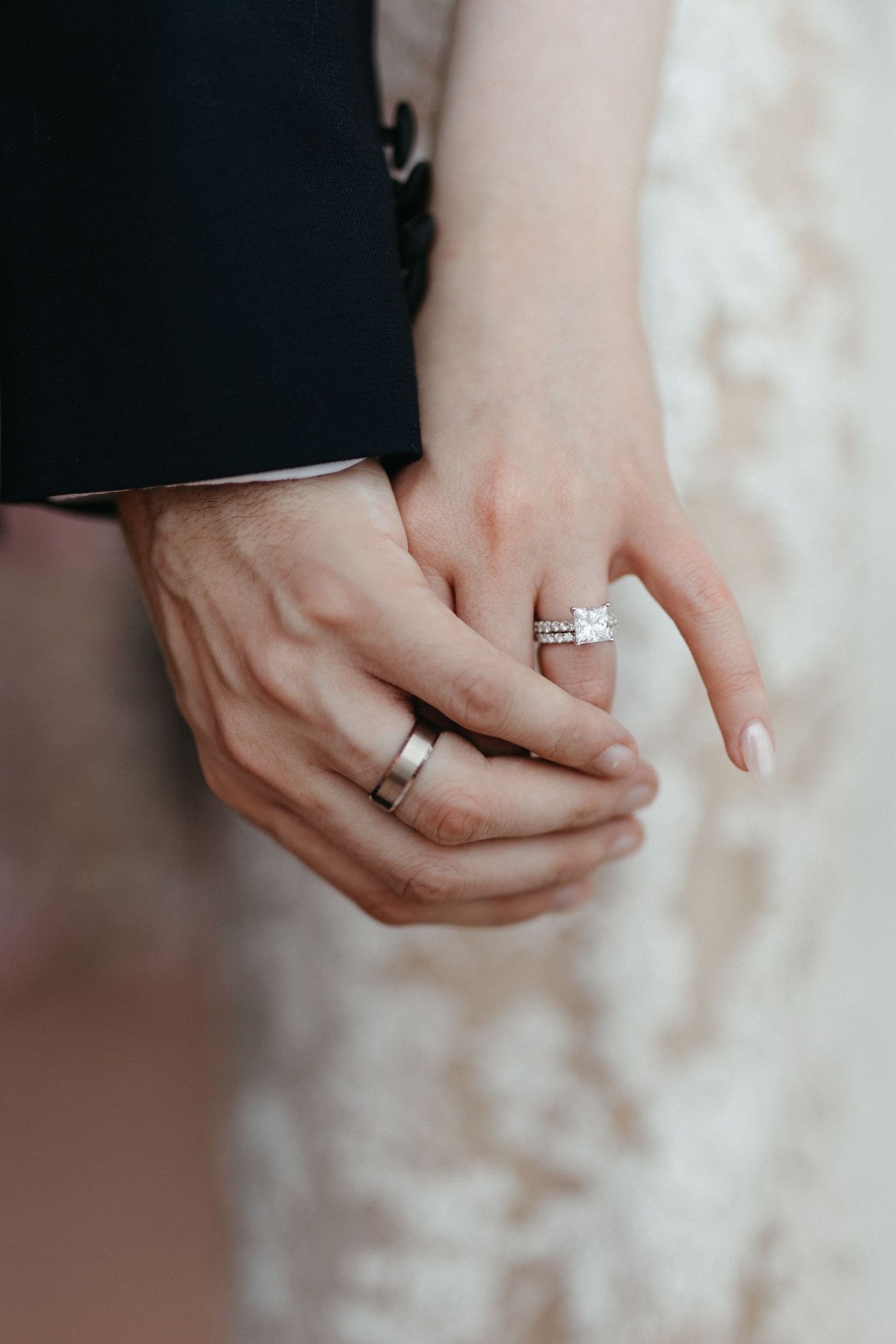 Close-up shot of hands wearing engagement ring and wedding band against light background.