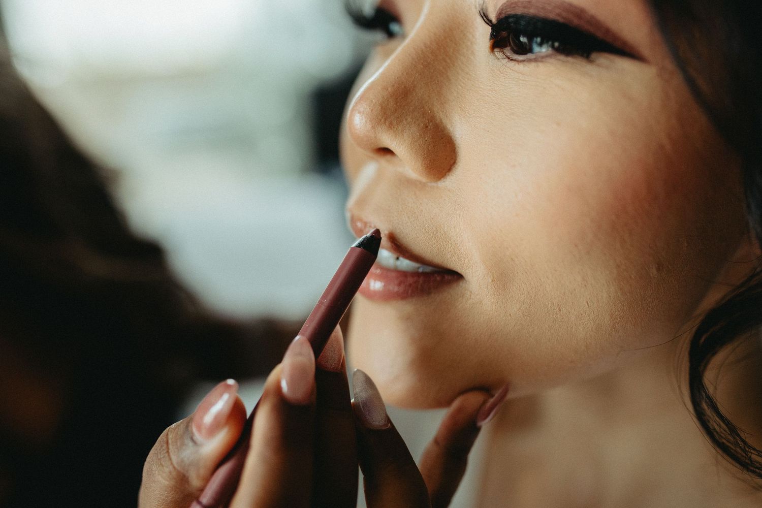 Closeup shot of makeup artist applying dark lipstick using a brush during professional beauty session.