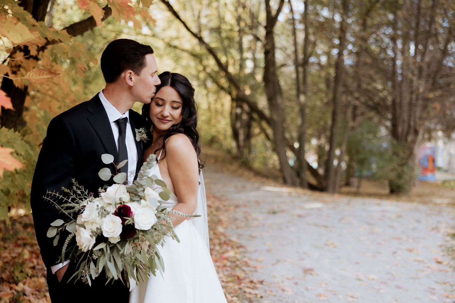 A couple poses with a white floral bouquet against fall foliage.