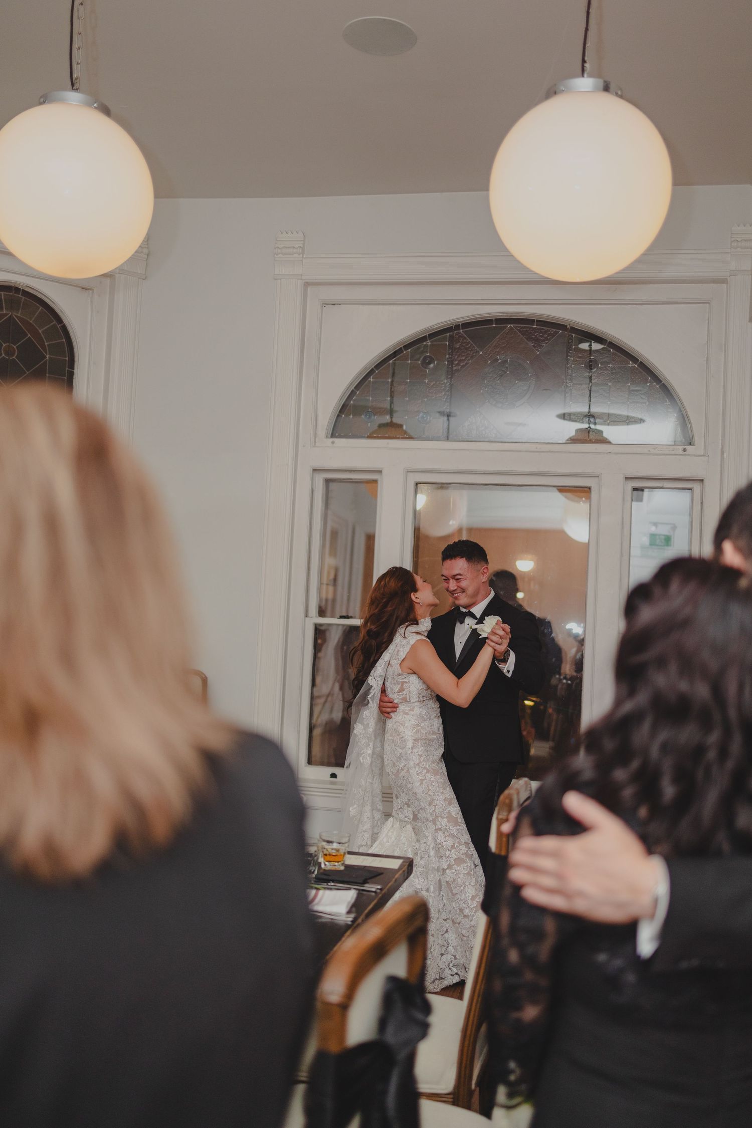 A couple shares their first dance as newlyweds in an elegant venue adorned with globe pendant lights.