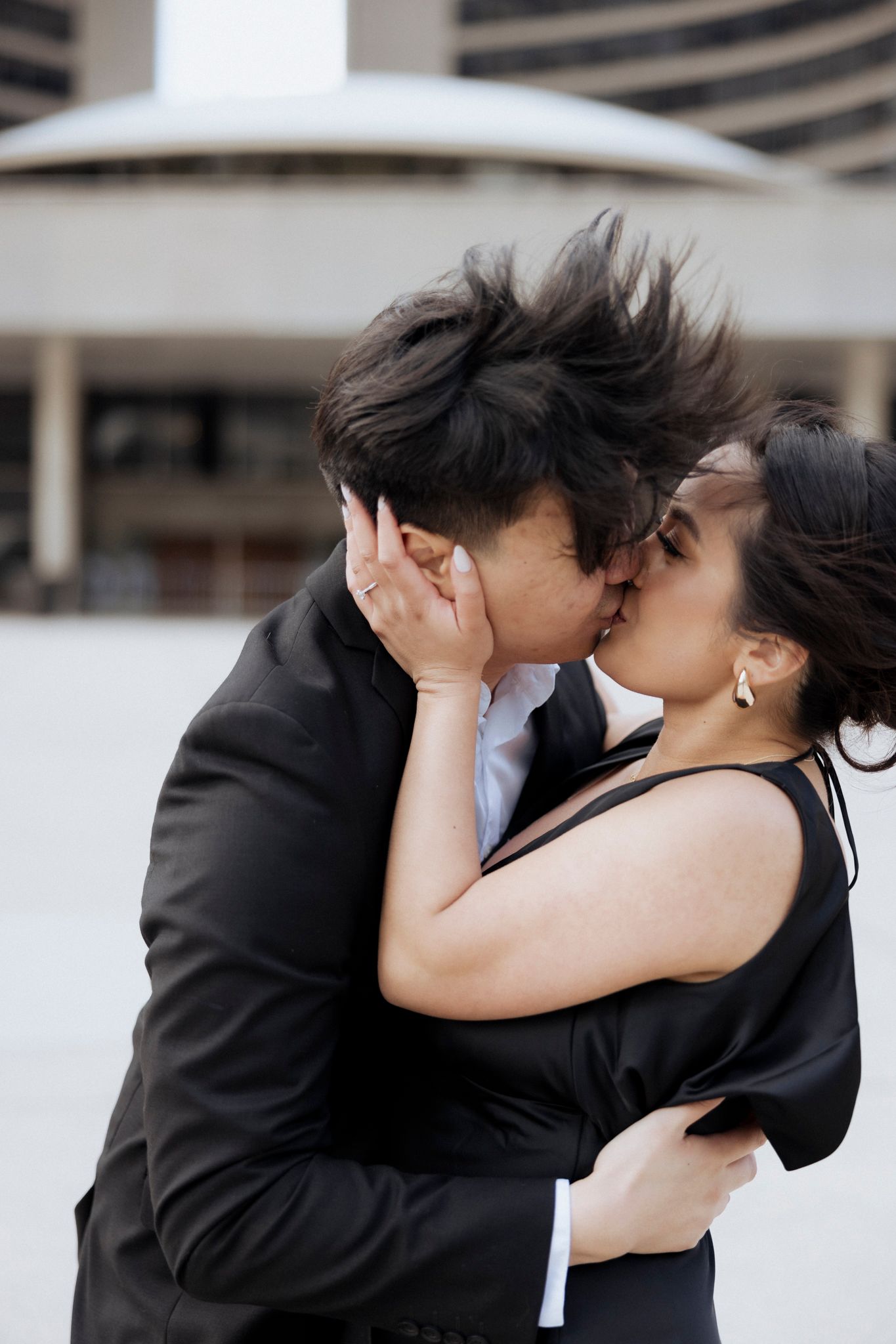 A tender moment shared between a couple in formal attire against a modern architectural background.
