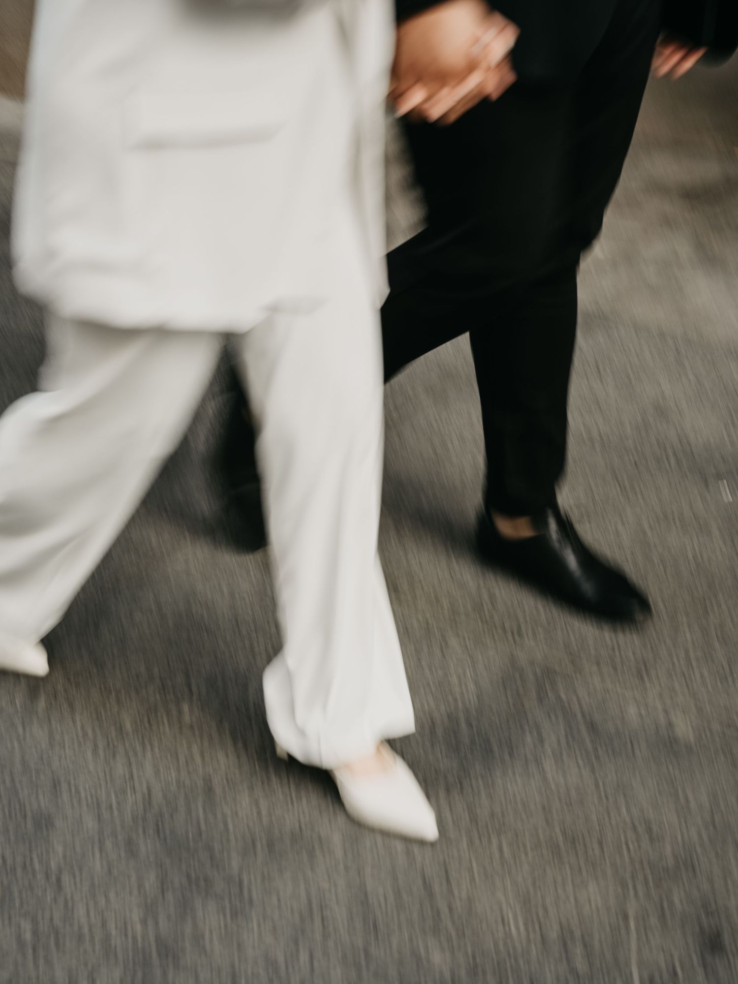 Motion blurred image of contrasting black and white outfits with focus on formal shoes walking on grey floor.