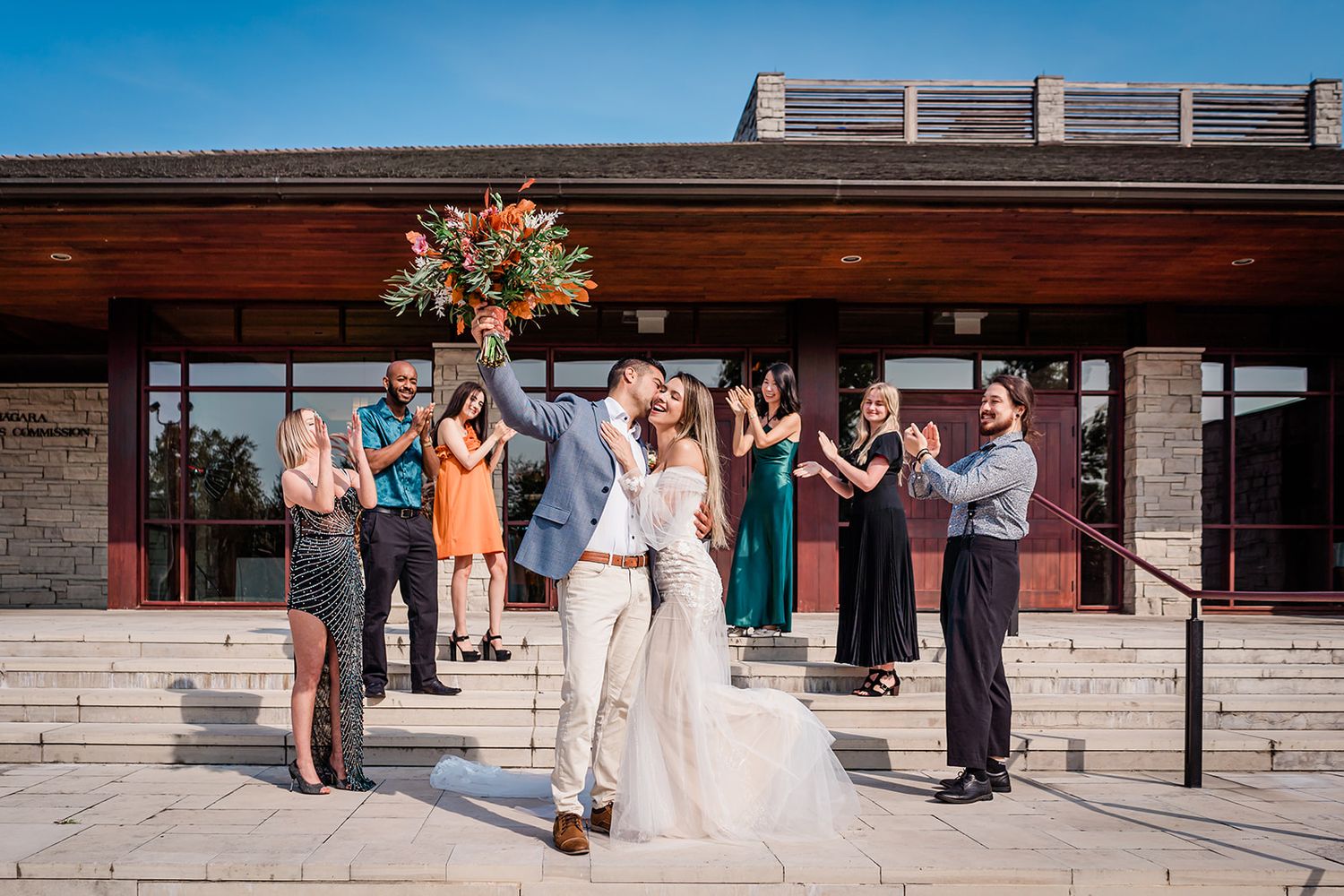 Wedding celebration outside modern building with guests cheering for newlyweds.