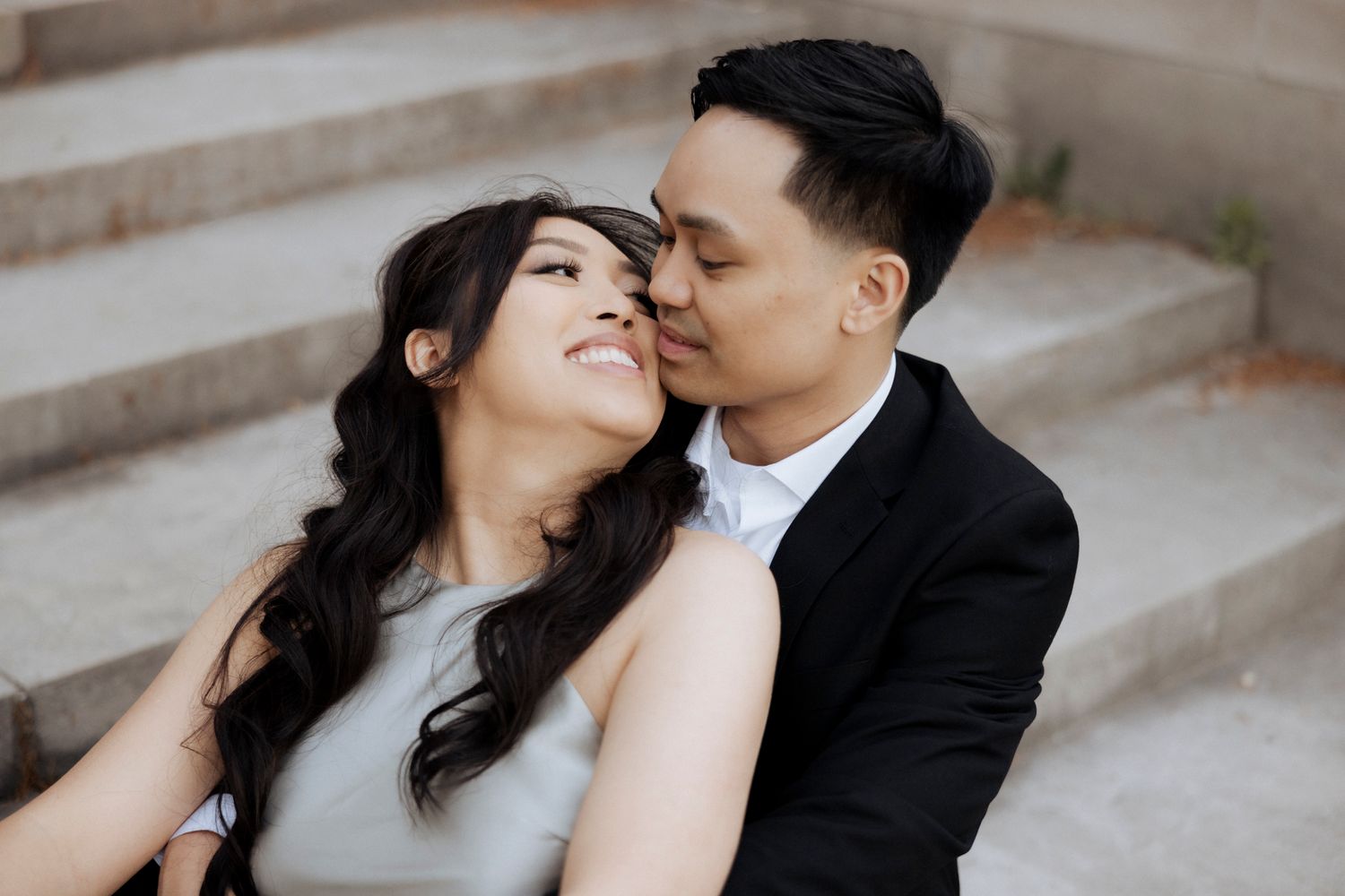 A couple shares an intimate moment while sitting on concrete steps outdoors.