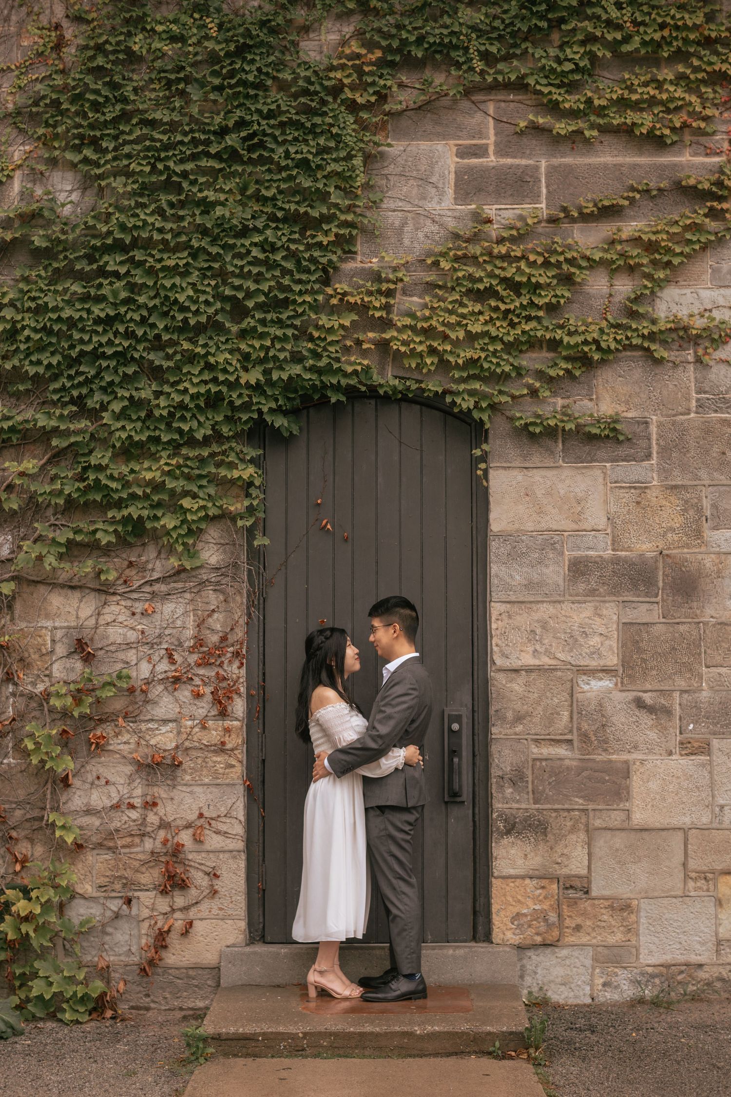 A couple embraces in a doorway framed by ivy-covered stone walls.
