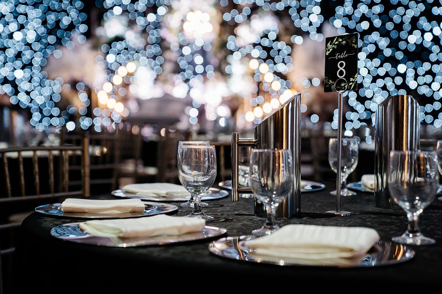 Elegant table setting with crystal glassware and bokeh lights creating a romantic atmosphere against dark tablecloth.