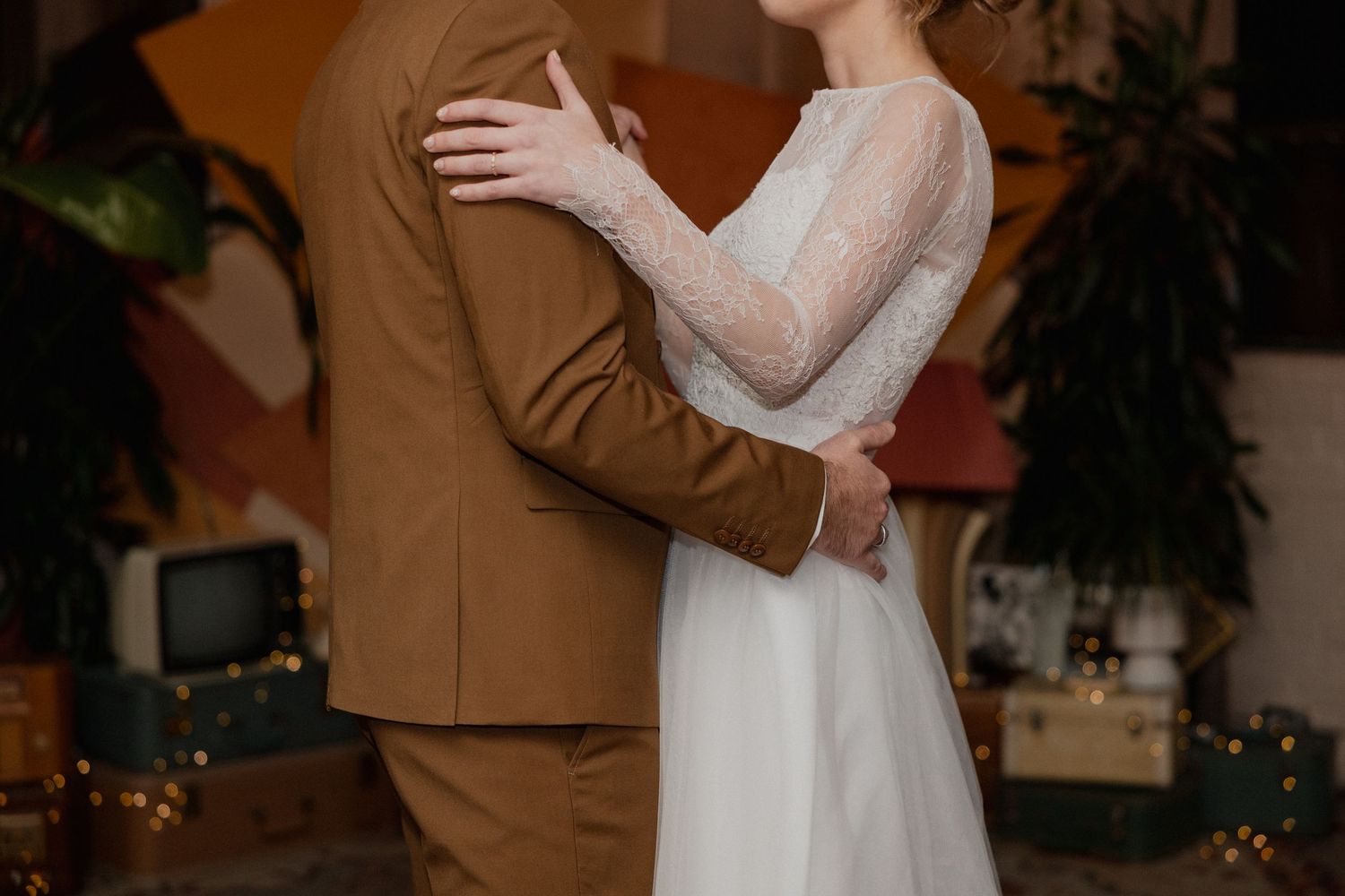 A couple in wedding attire embrace during a romantic indoor ceremony with warm lighting and decorative plants.