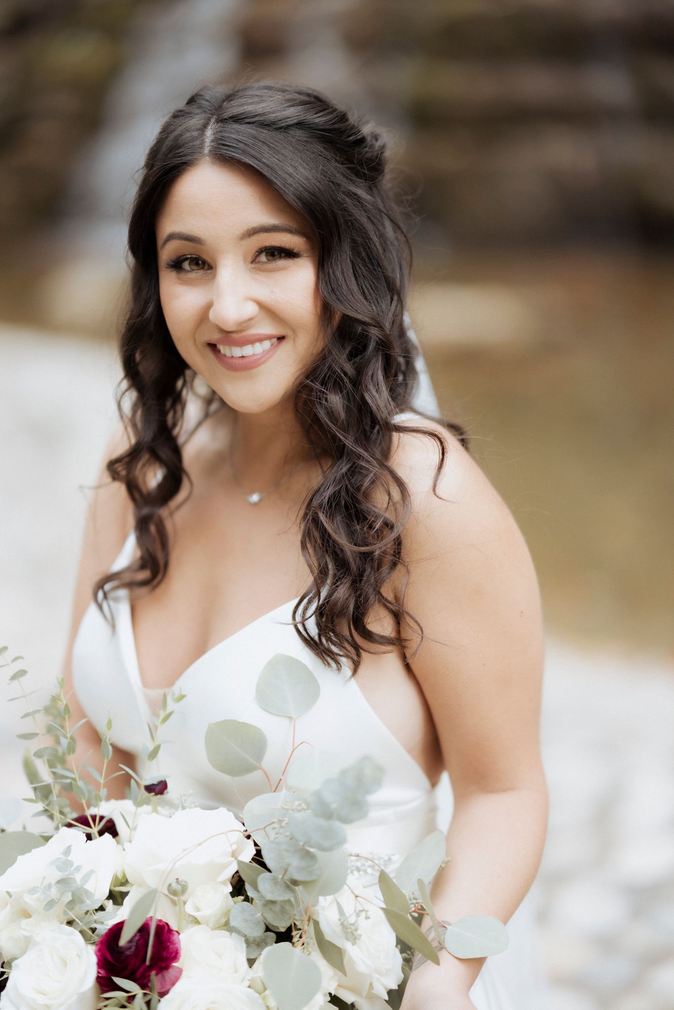 Bride holding a beautiful bouquet of white and burgundy flowers against a neutral background.