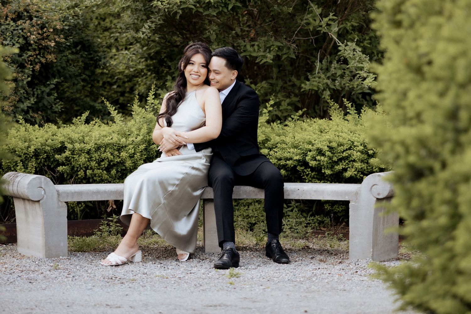 Couple sharing intimate moment on stone bench surrounded by lush garden scenery.