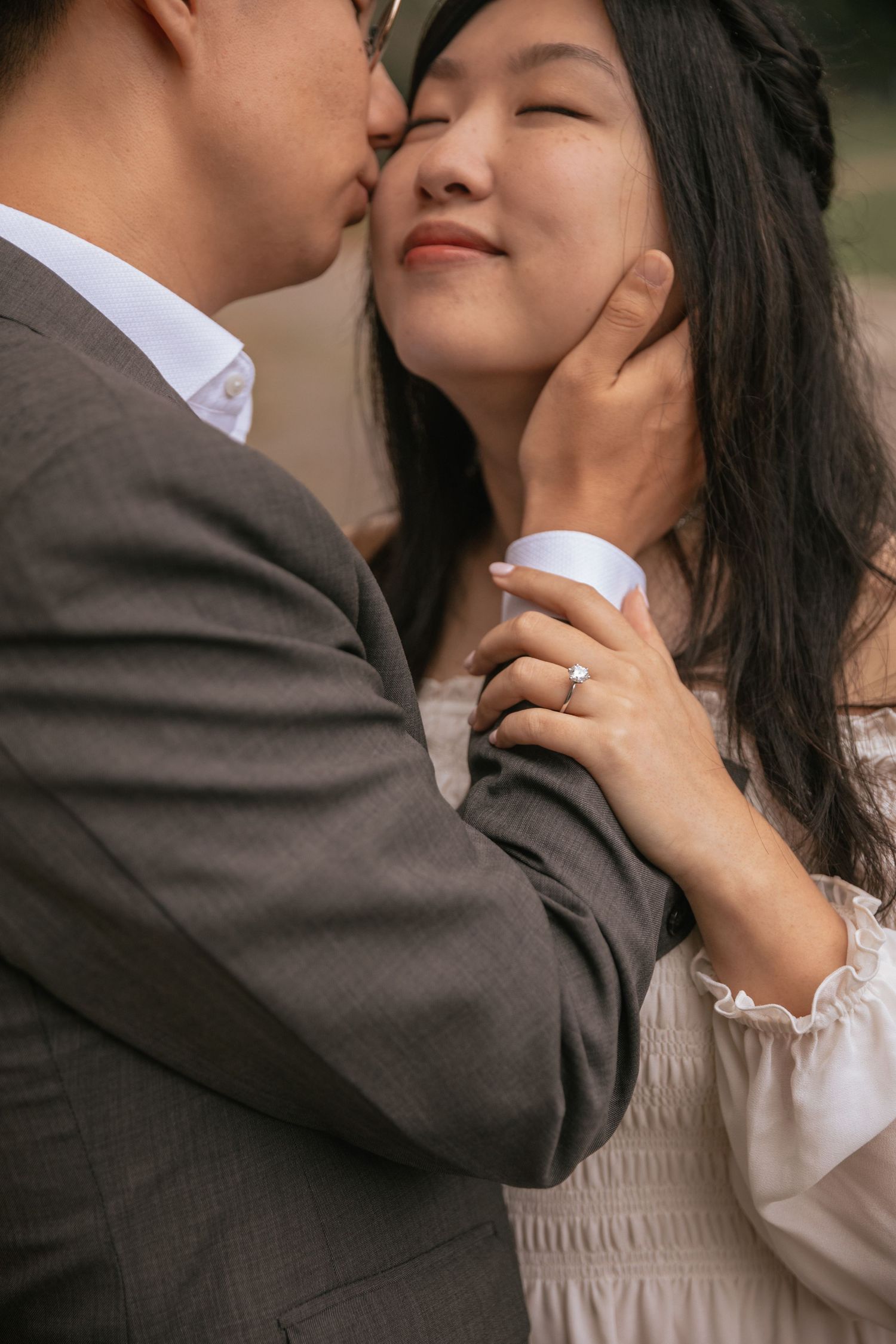 A romantic couple shares an intimate moment outdoors, with gentle hands and soft expressions showing their affection.