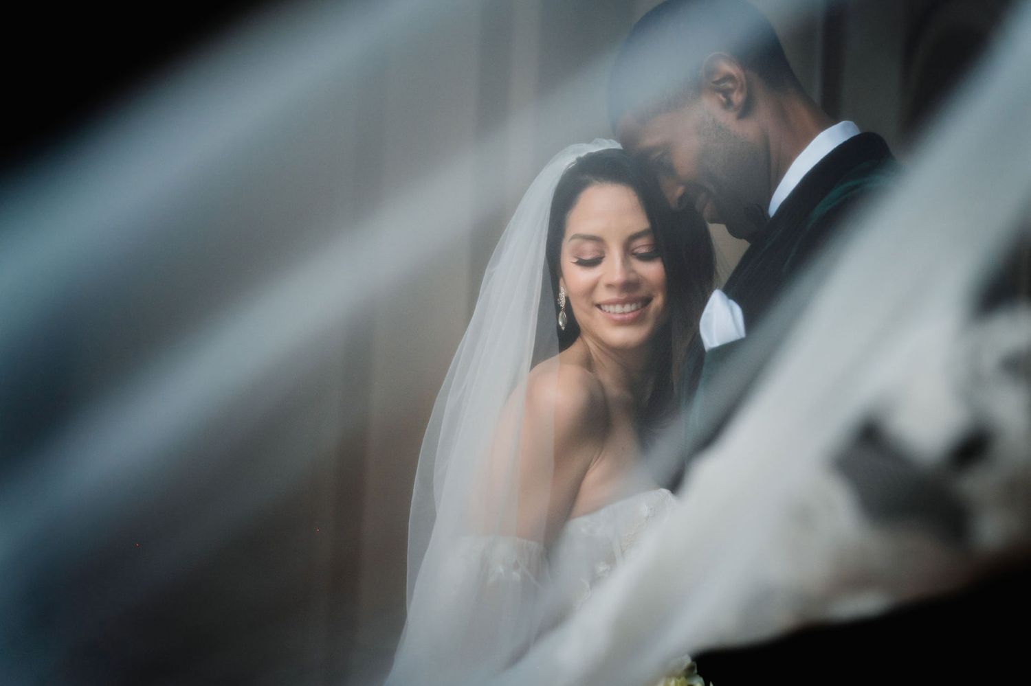 A soft focus wedding portrait through sheer fabric creating a dreamy, romantic effect.
