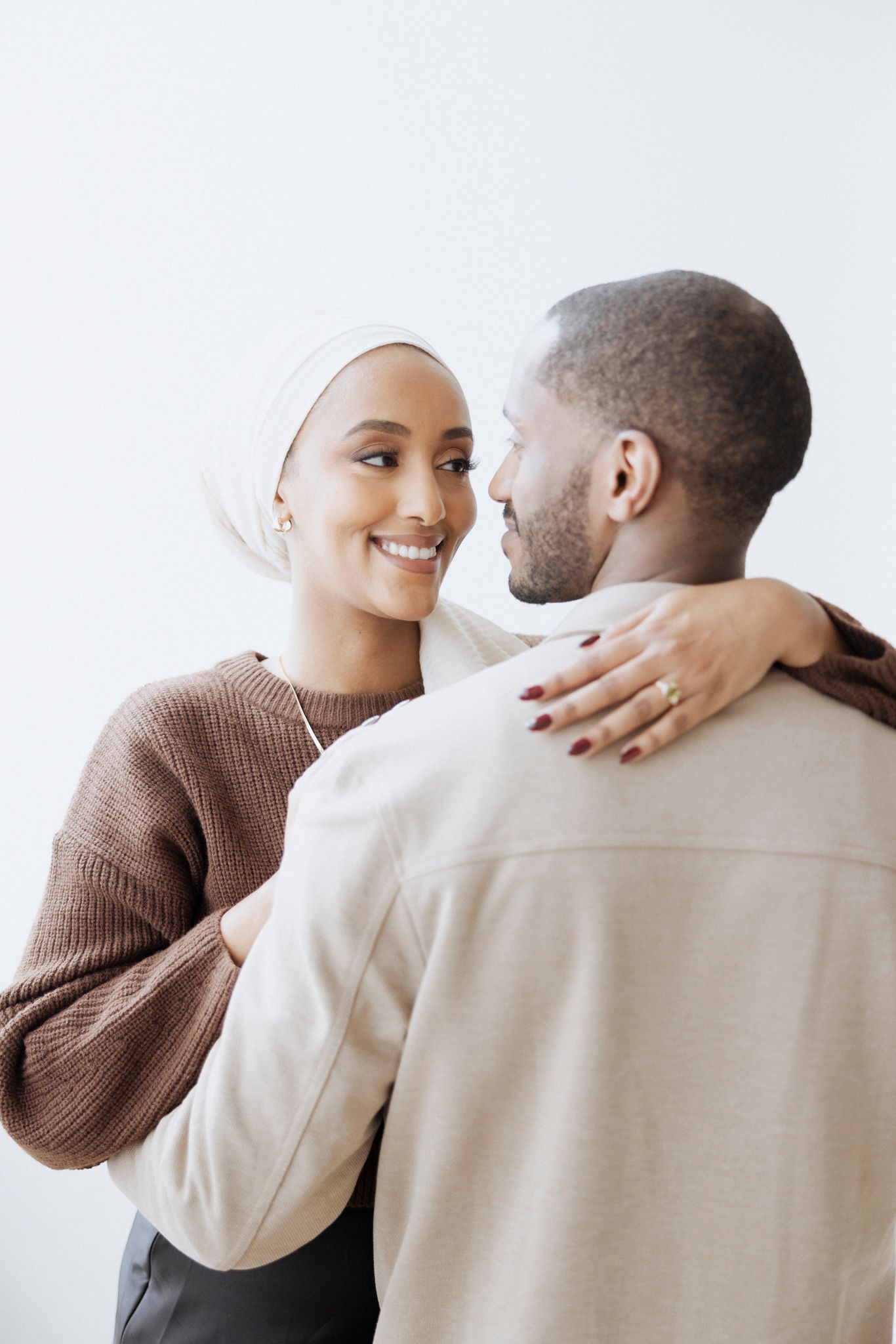 An affectionate couple embraces while wearing cozy sweaters against a white background.