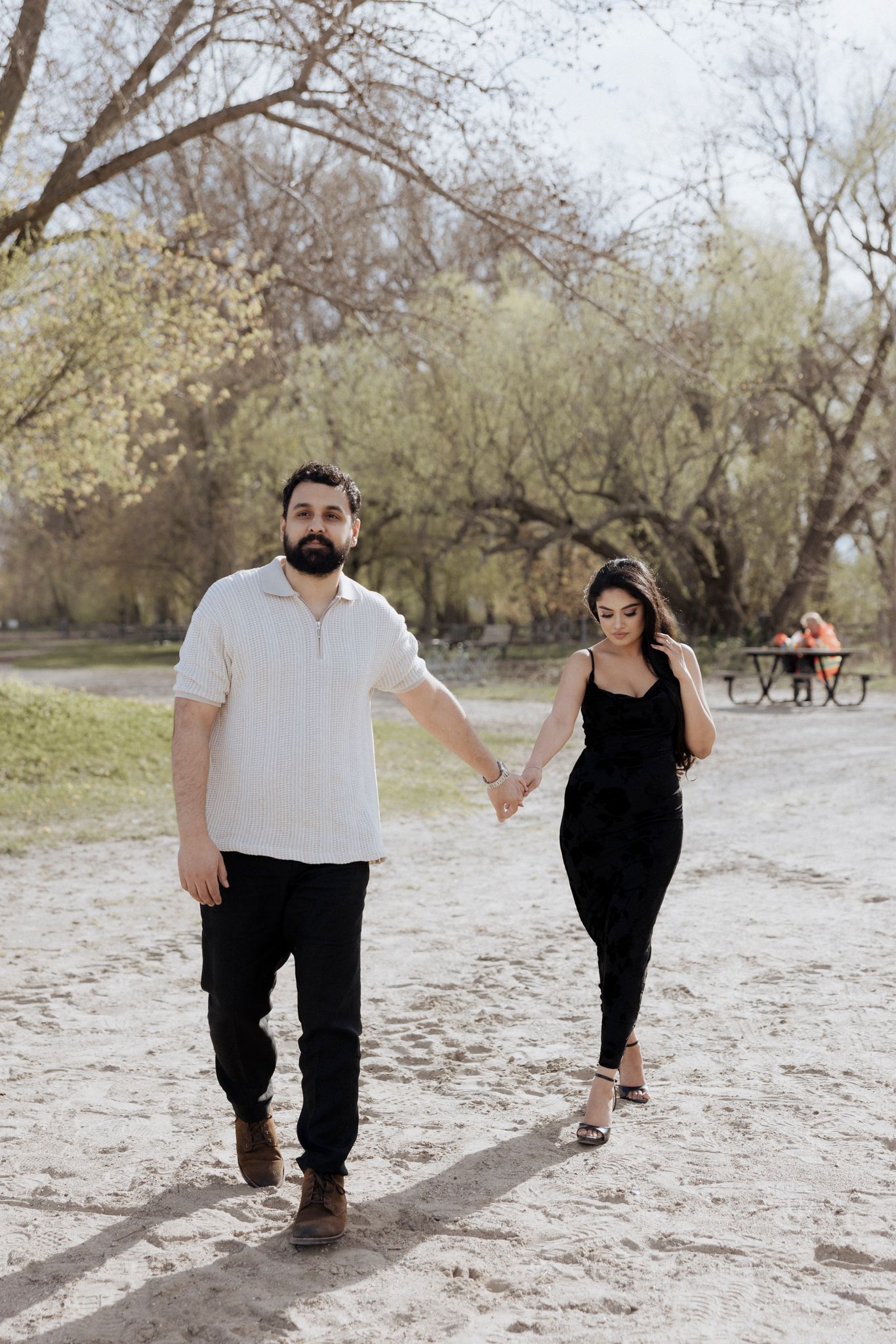 A couple walks hand in hand along a nature trail with bare trees in the background.