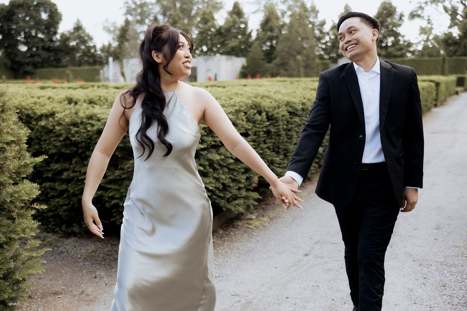 A couple in wedding attire walk hand-in-hand along a garden path on their special day.