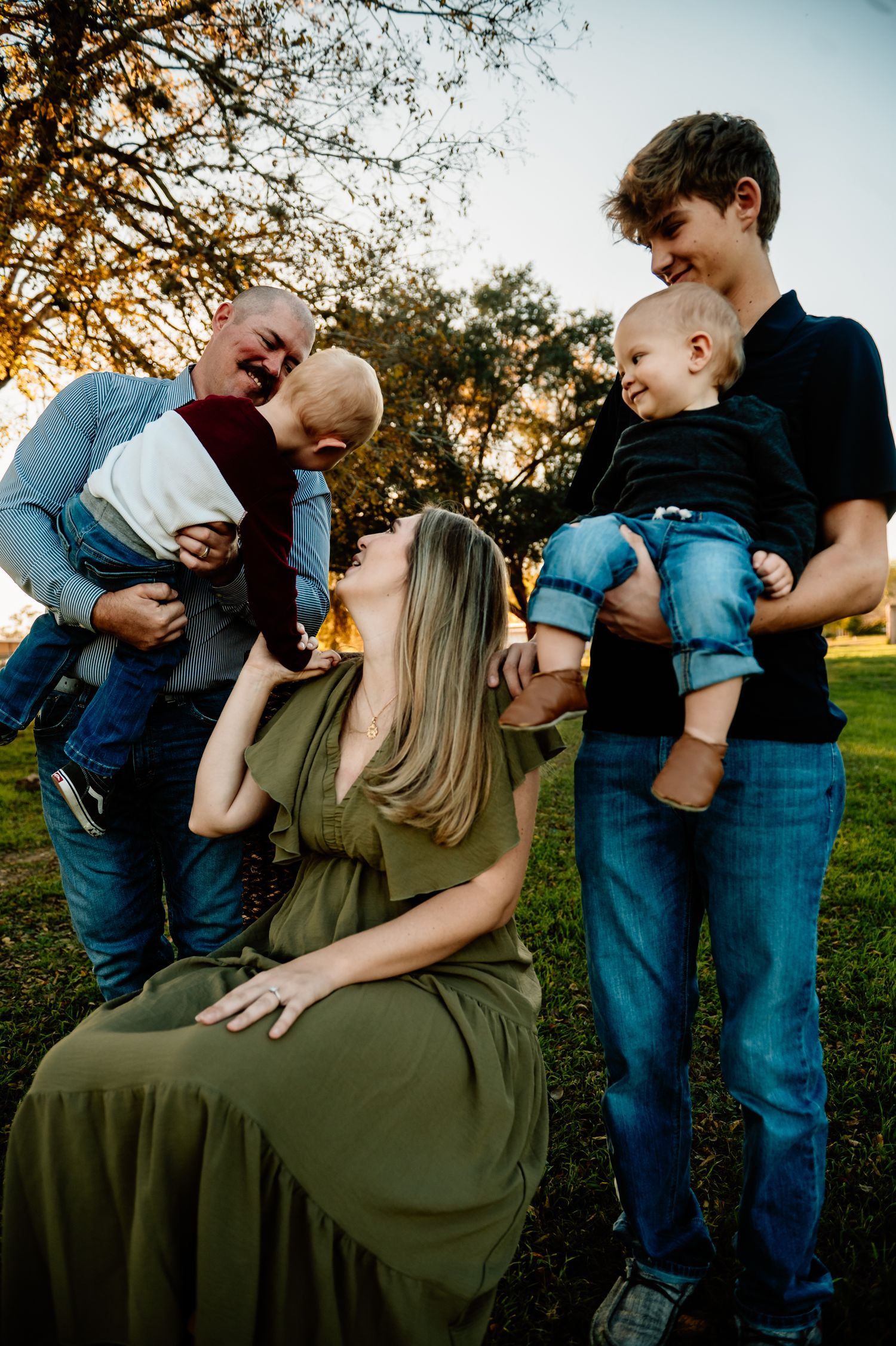 Family with young children shares joyful moment outdoors during golden hour sunset.