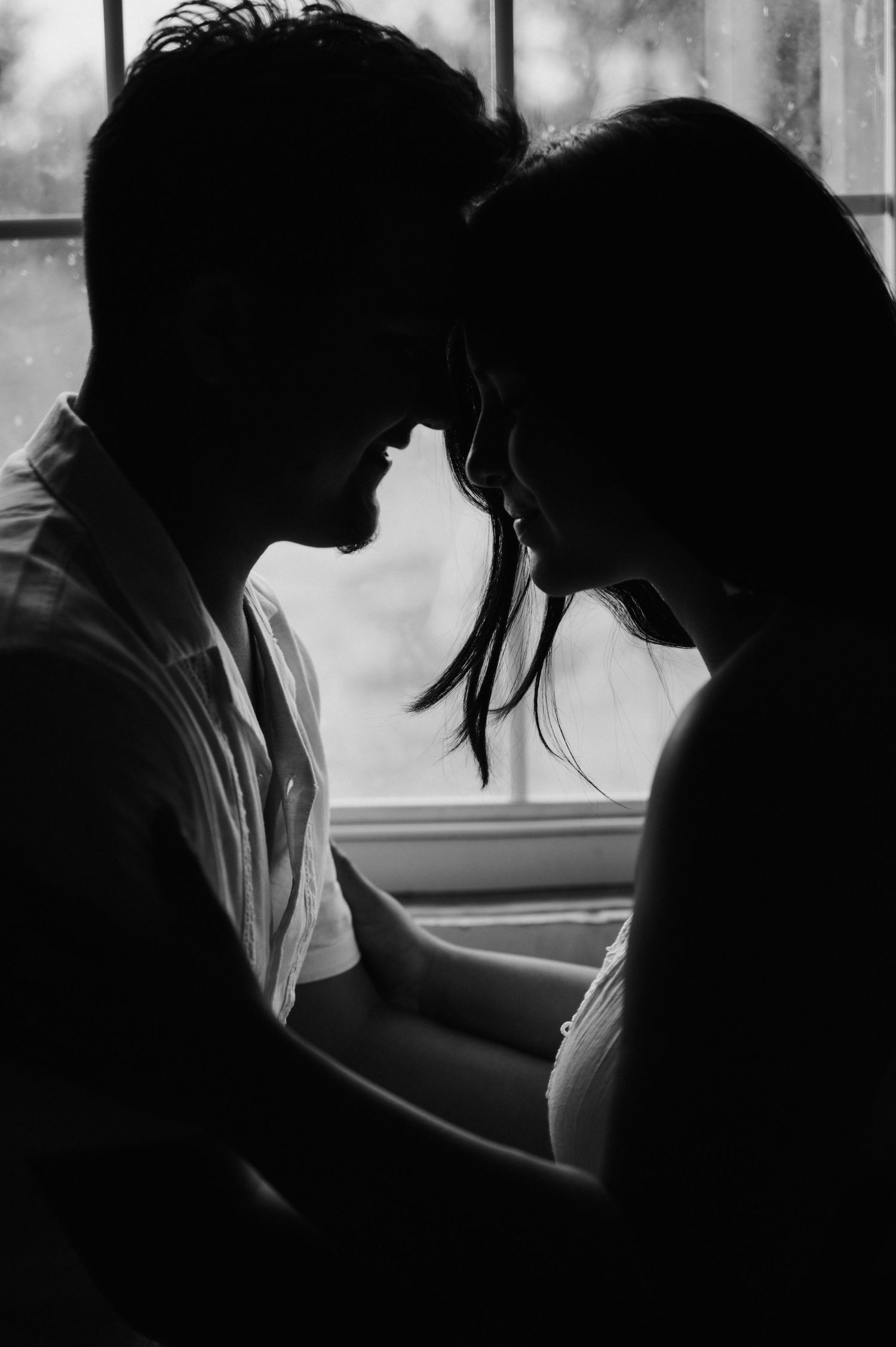 Silhouette of a romantic couple in an intimate moment by a window backlit in black and white.