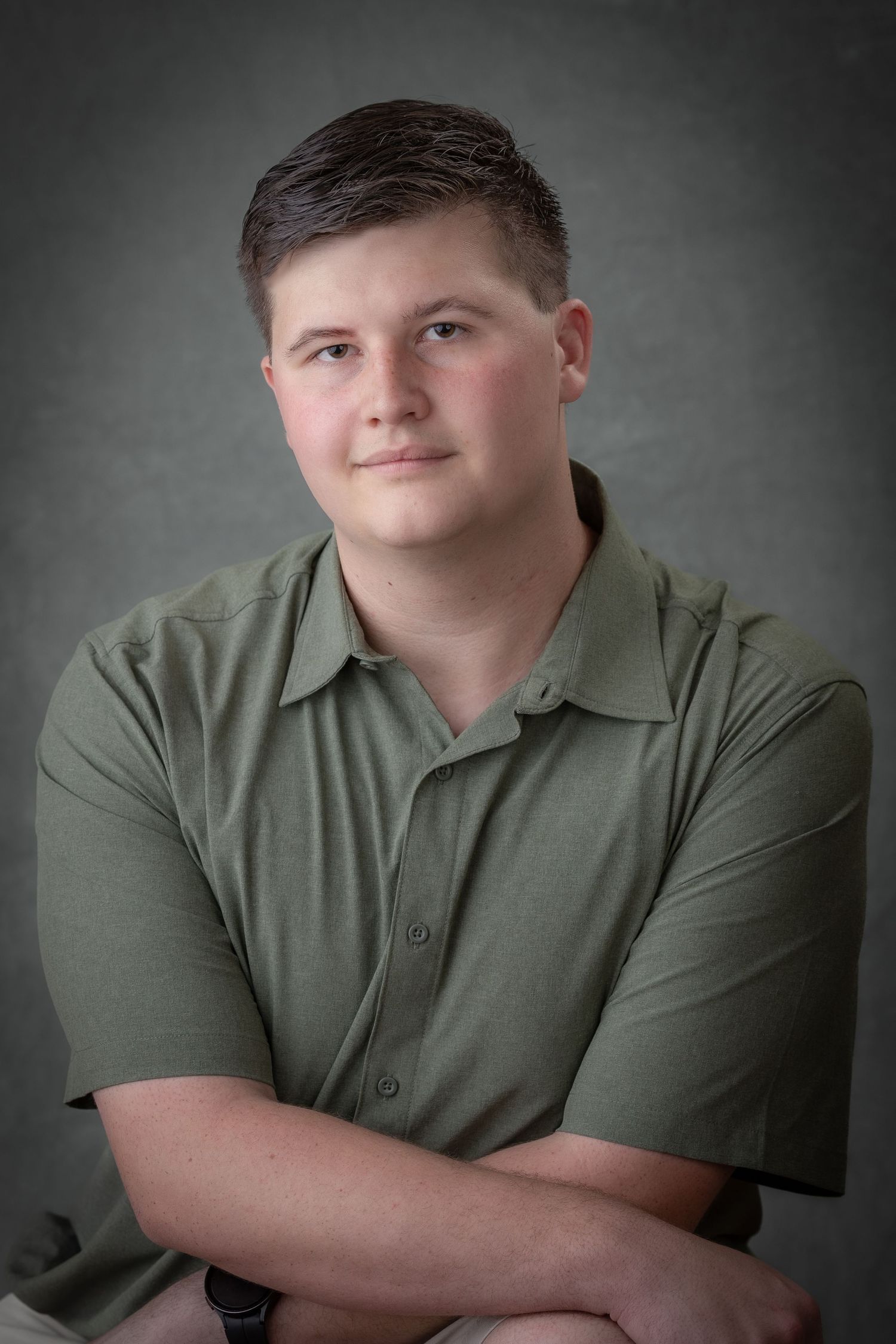 Professional portrait of someone in olive polo with arms crossed against grey backdrop.