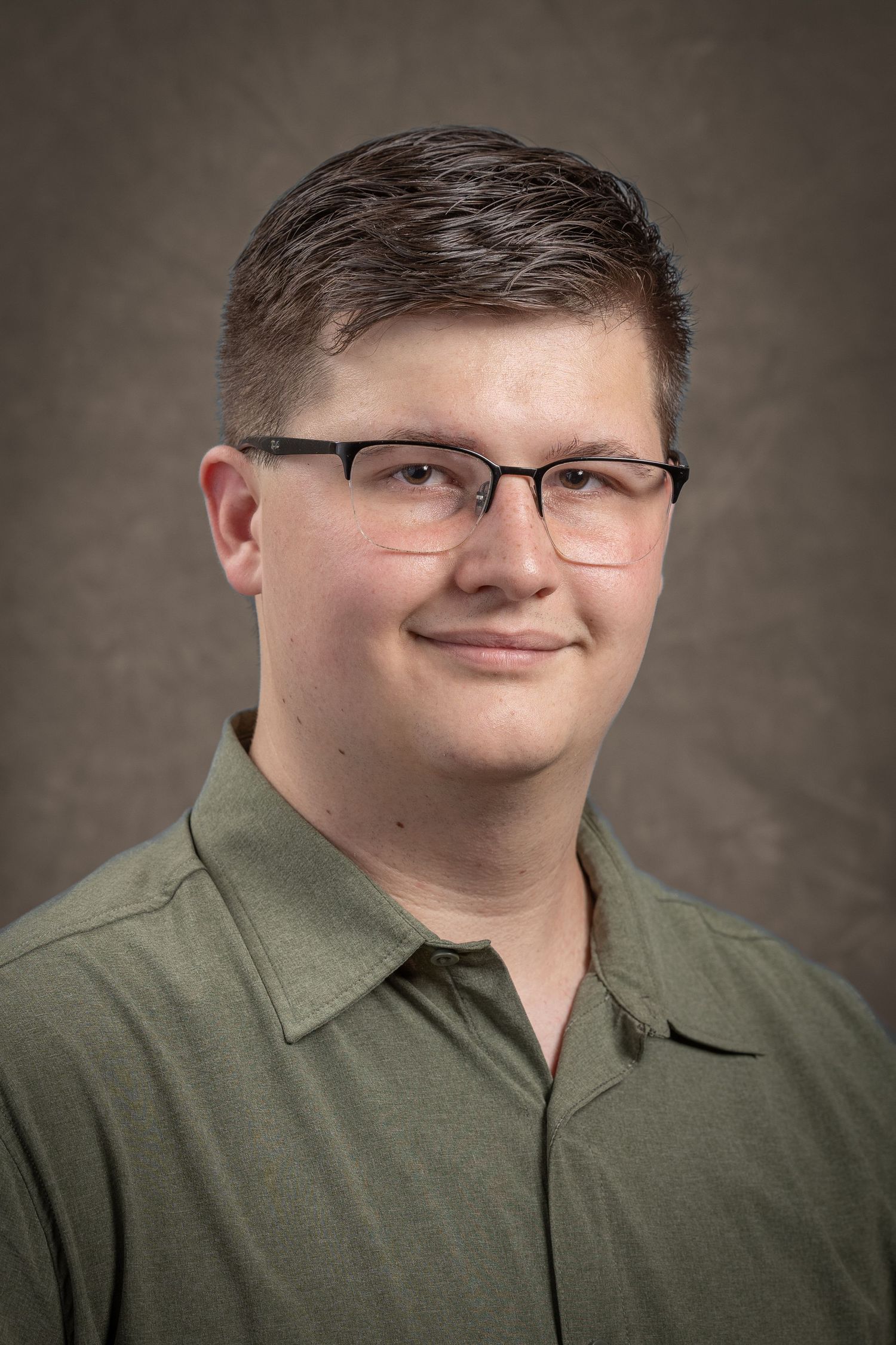 Studio portrait of someone wearing glasses and olive shirt against neutral backdrop.
