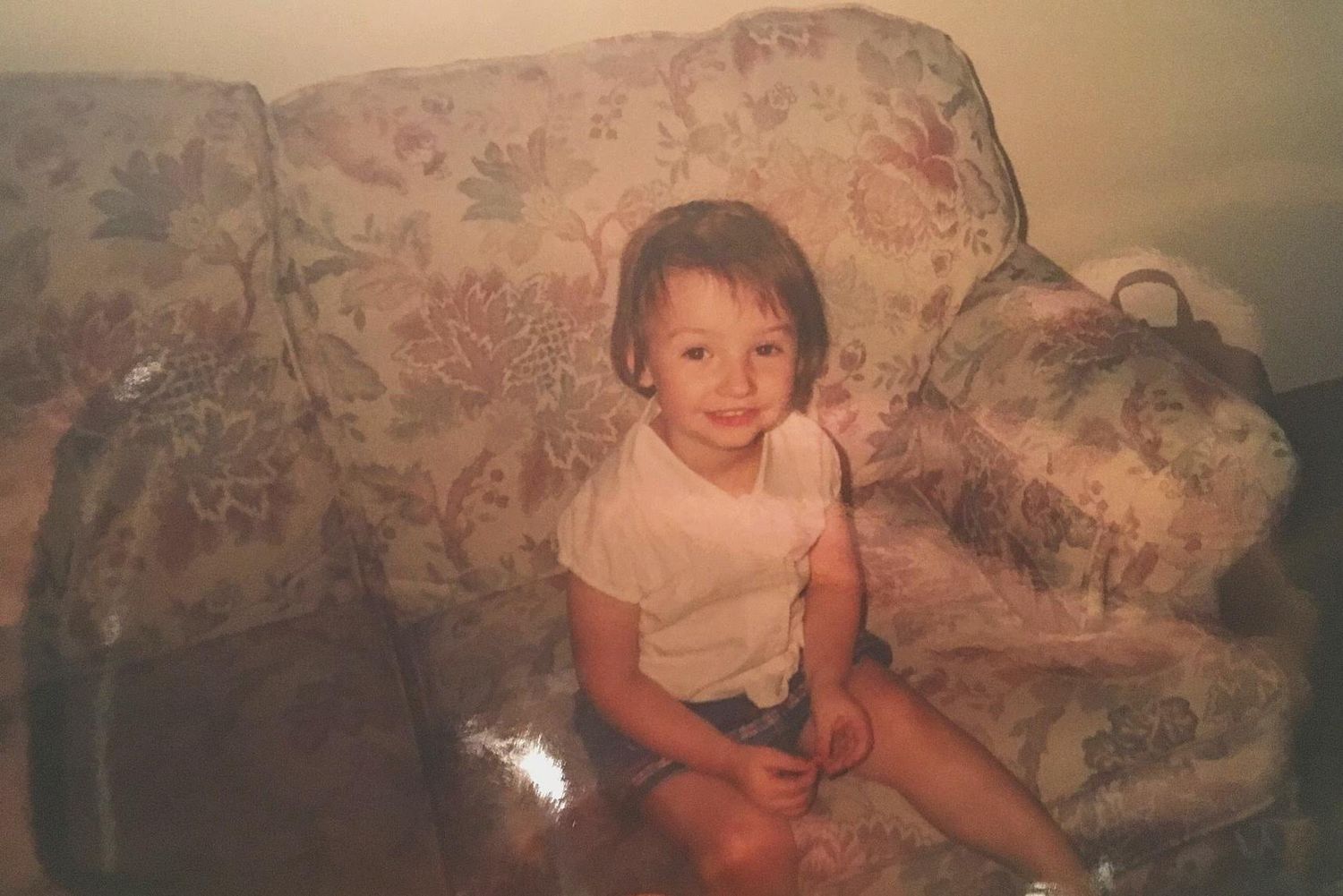Small toddler sitting on a floral patterned couch in vintage photograph.