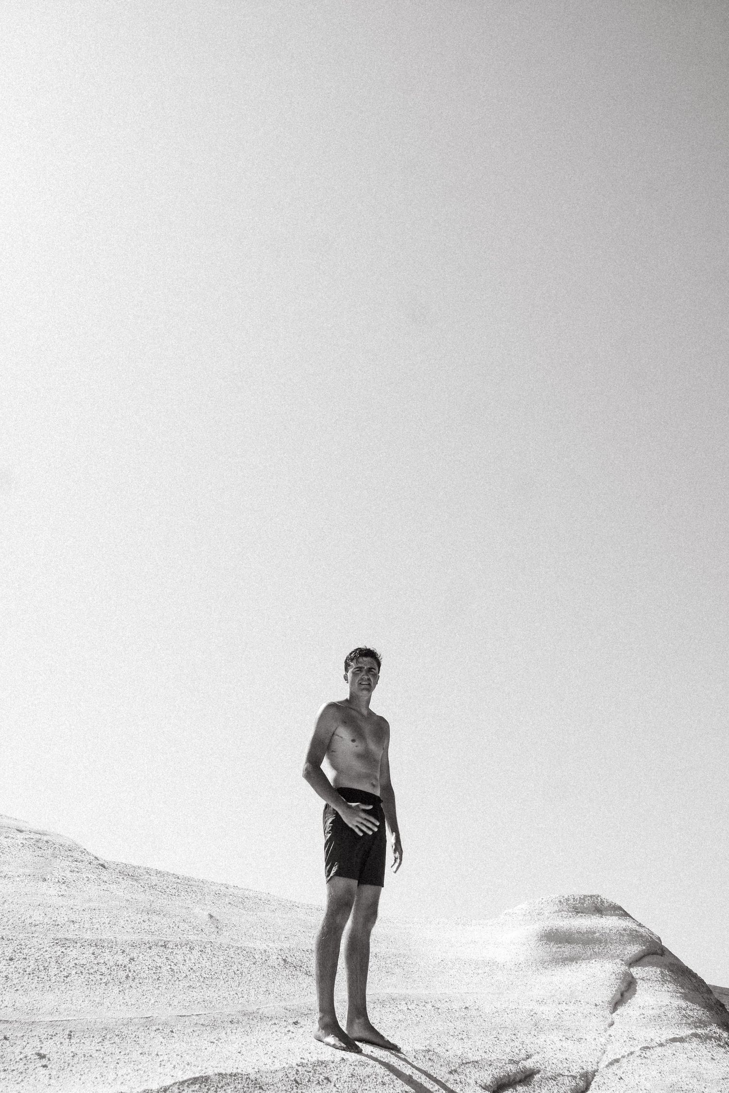A black and white photo of someone standing on a sandy hill against a bright sky.