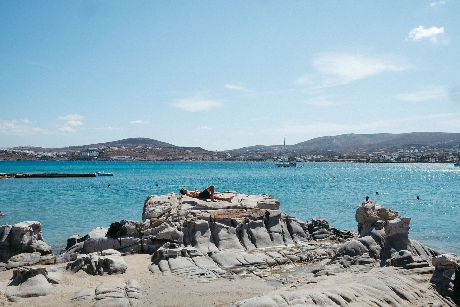 Rocky coastline with turquoise waters and mountains in the background on a sunny Mediterranean day.