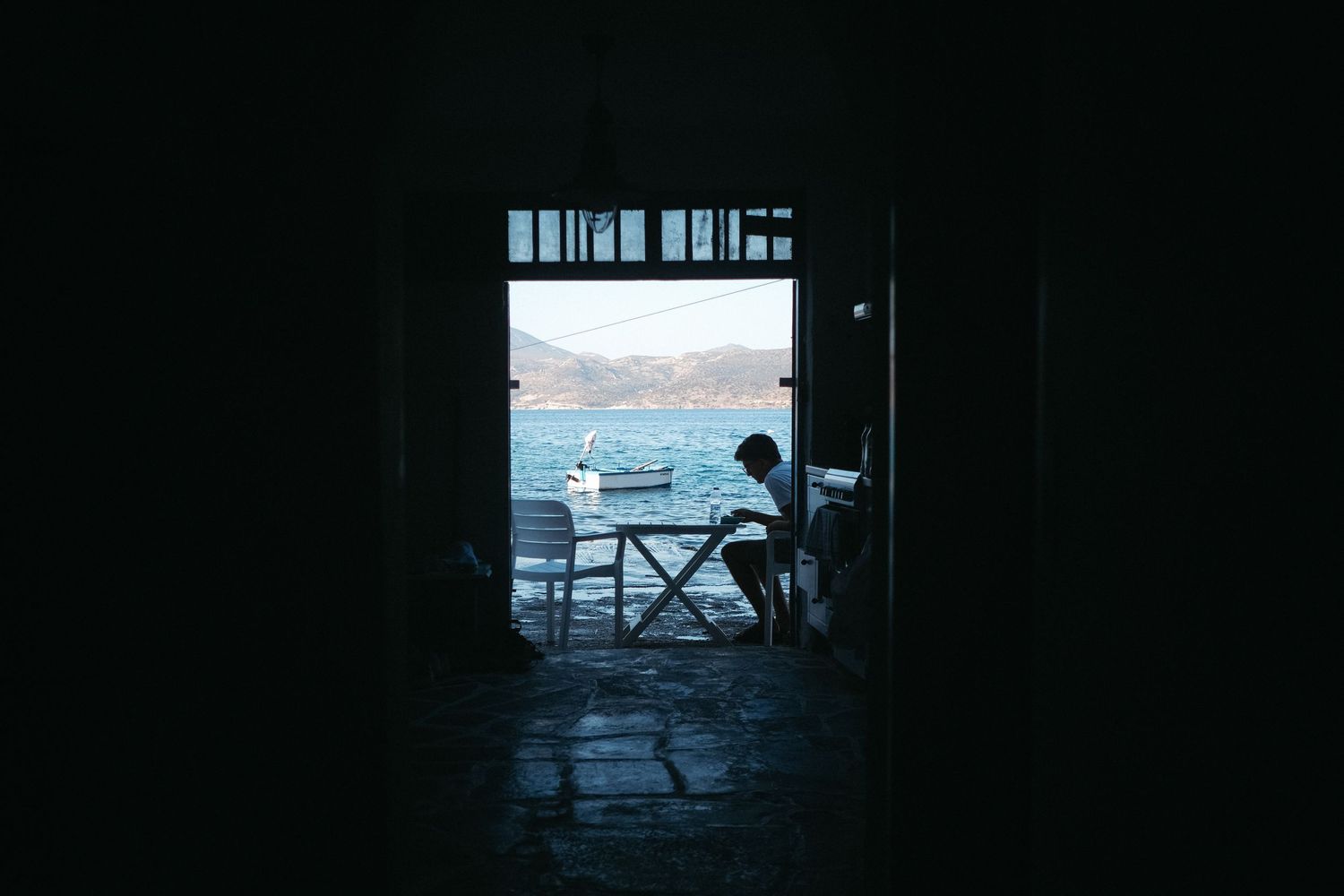 Silhouetted figure framed in doorway overlooking Mediterranean sea.
