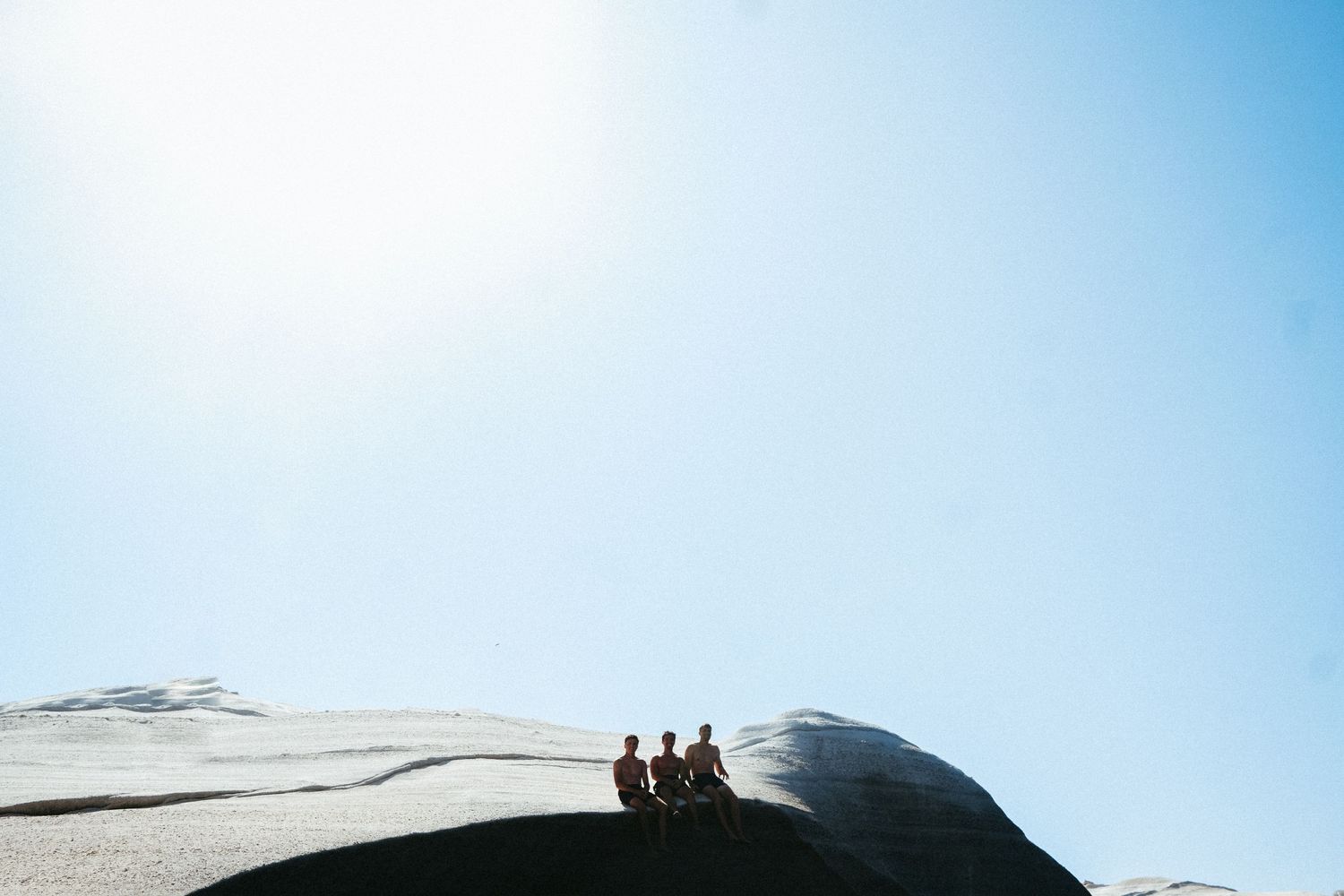 Silhouettes of people sitting atop a white rock formation against a bright blue sky.