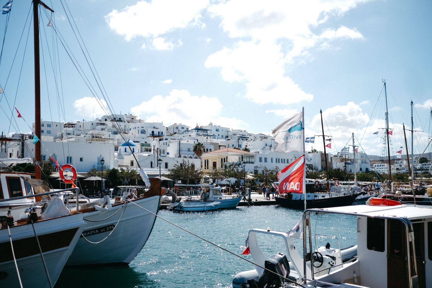 Boats docked in a Mediterranean harbor with white hillside buildings in the background.