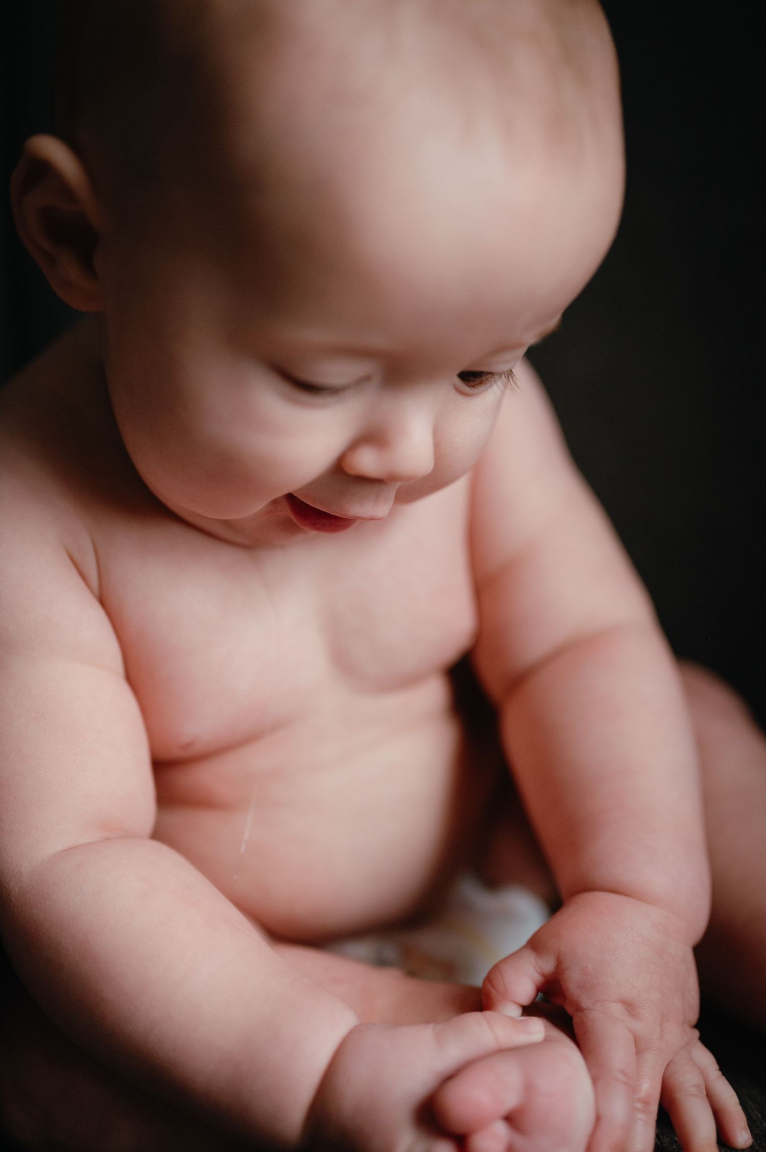Smiling baby sitting in dramatic lighting during intimate portrait session.