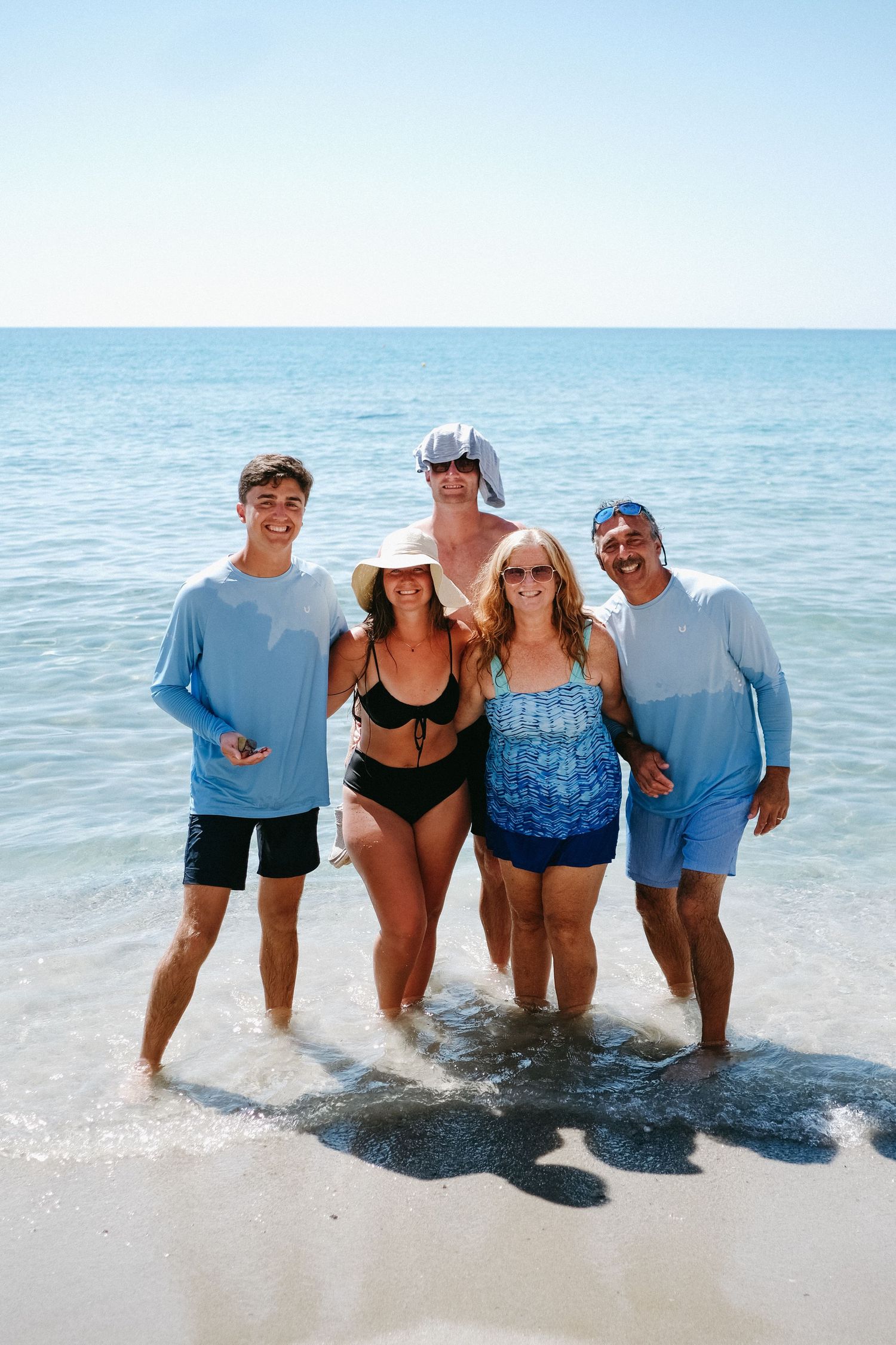A group of friends enjoying a summer day at the beach with crystal clear blue waters in the background.