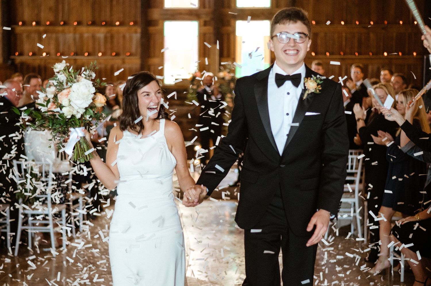 Newlyweds celebrate with confetti during their elegant barn wedding reception.