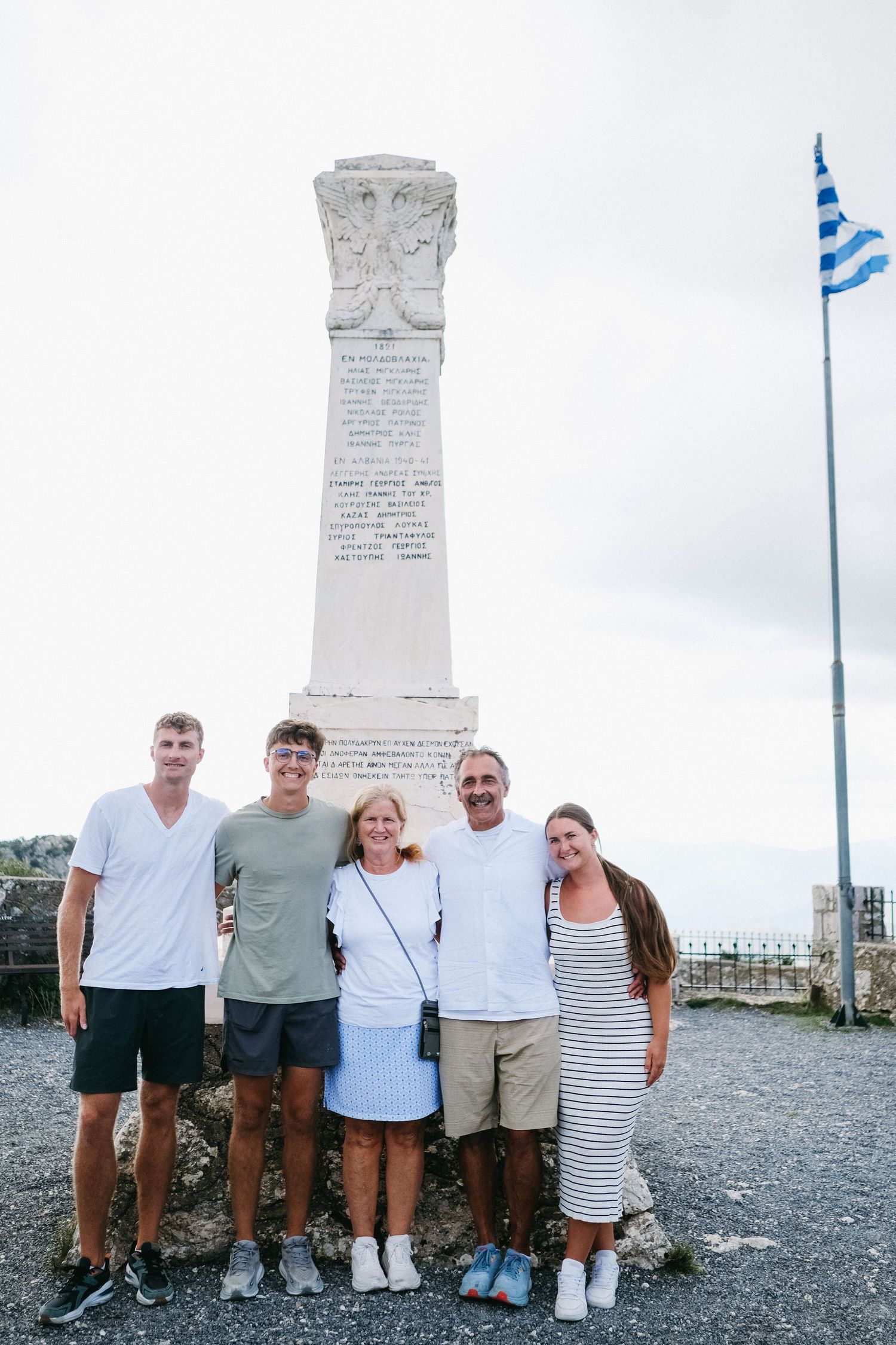 Group posing by a monument with Greek flag flying in the background.