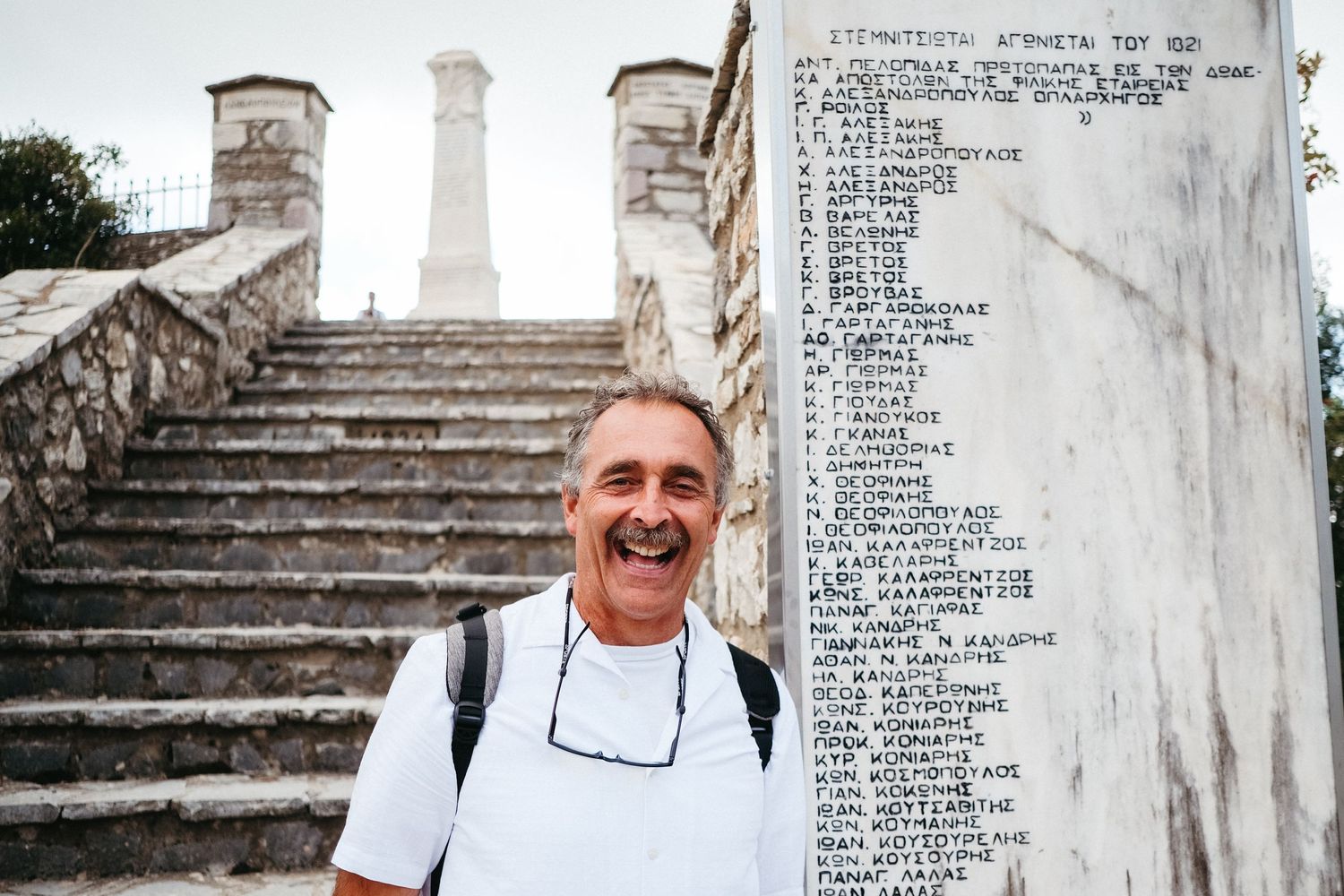 A tourist poses next to a historic monument with text inscriptions on stone steps.