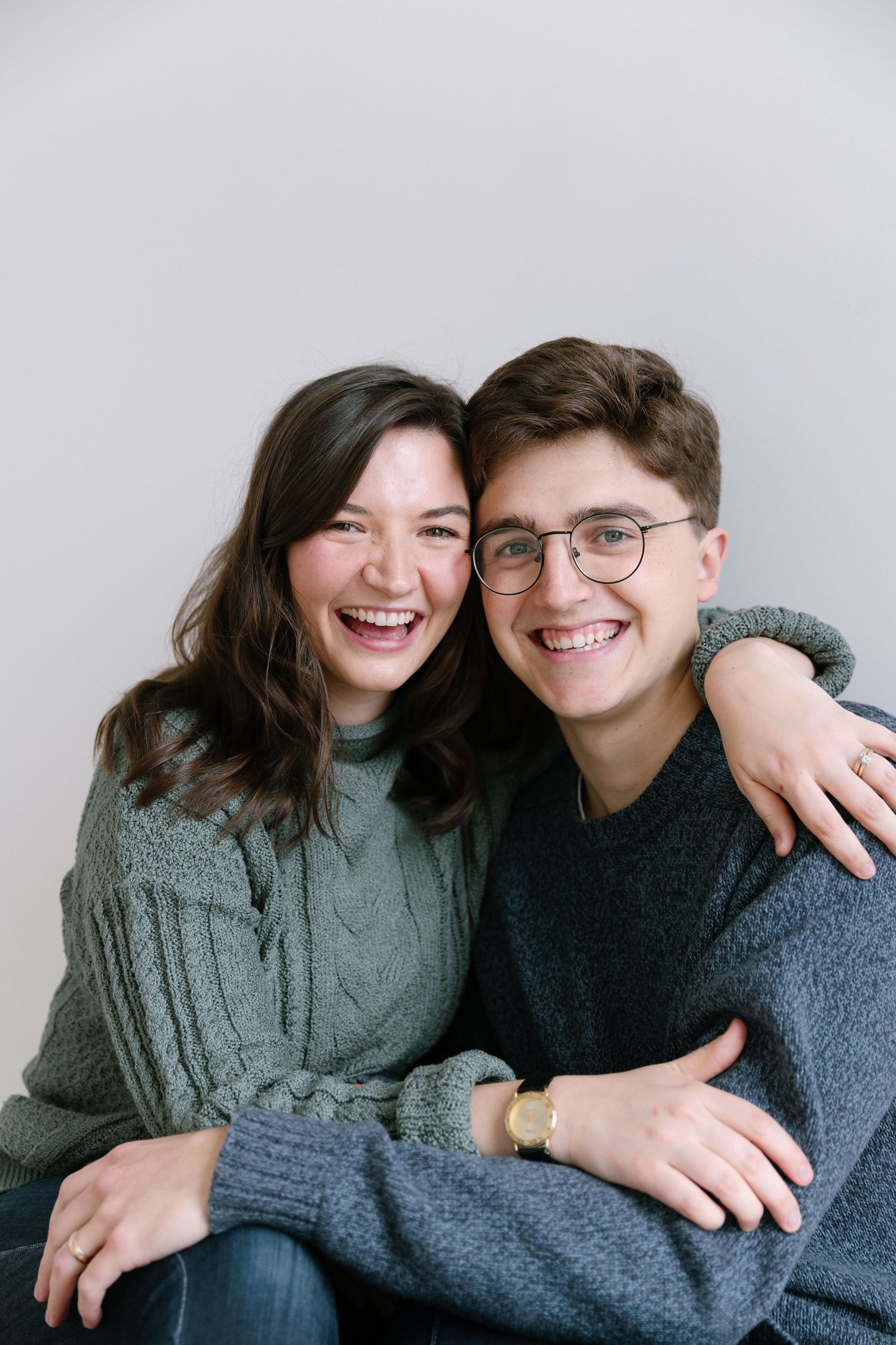 Two people in gray sweaters sharing a joyful moment against a white background.