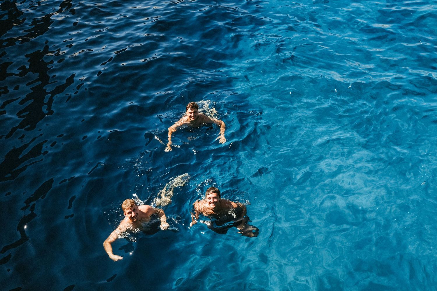 People swimming and floating in crystal clear blue Mediterranean waters.