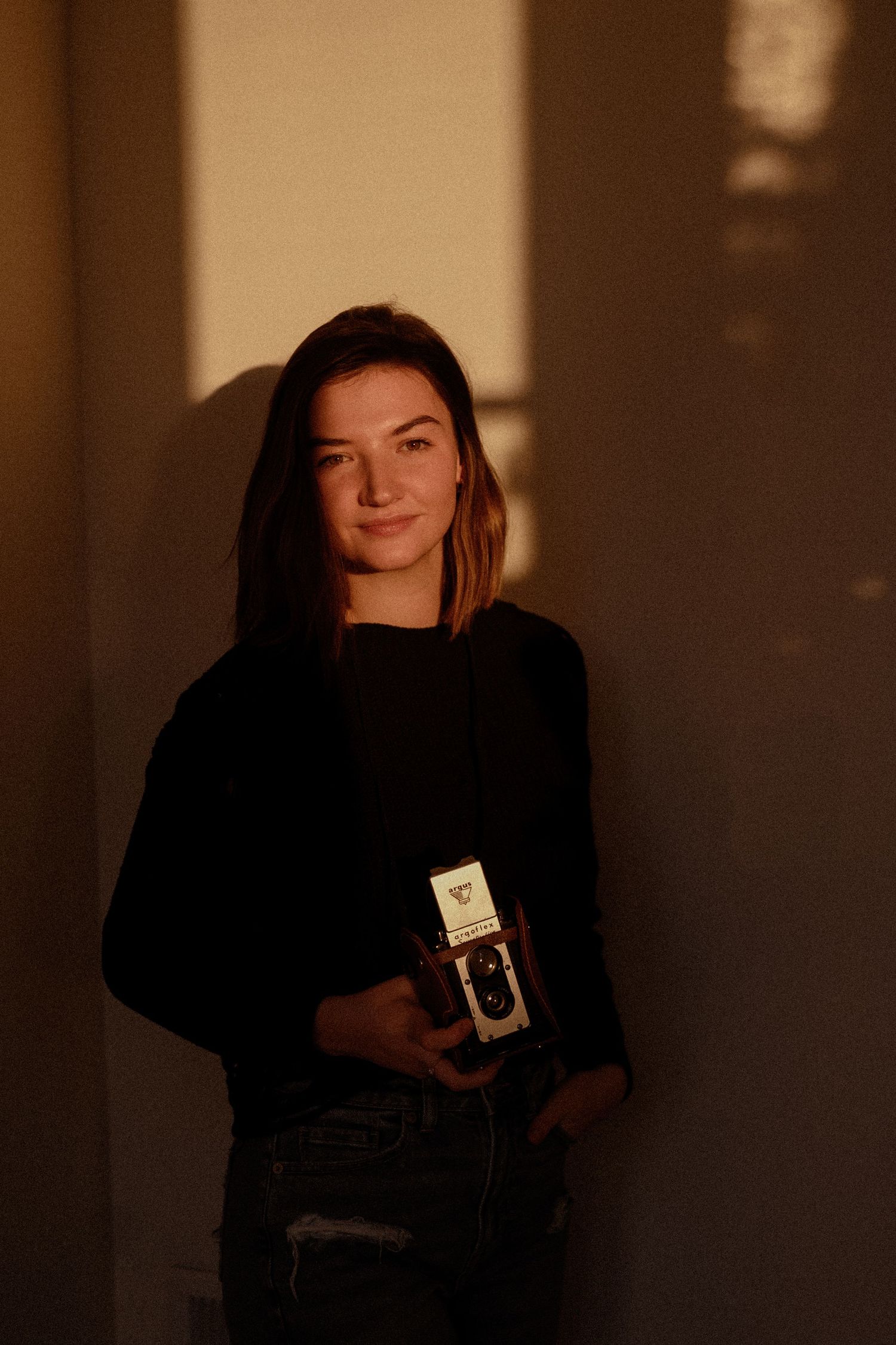 Moody portrait of person holding vintage camera in warm lighting.