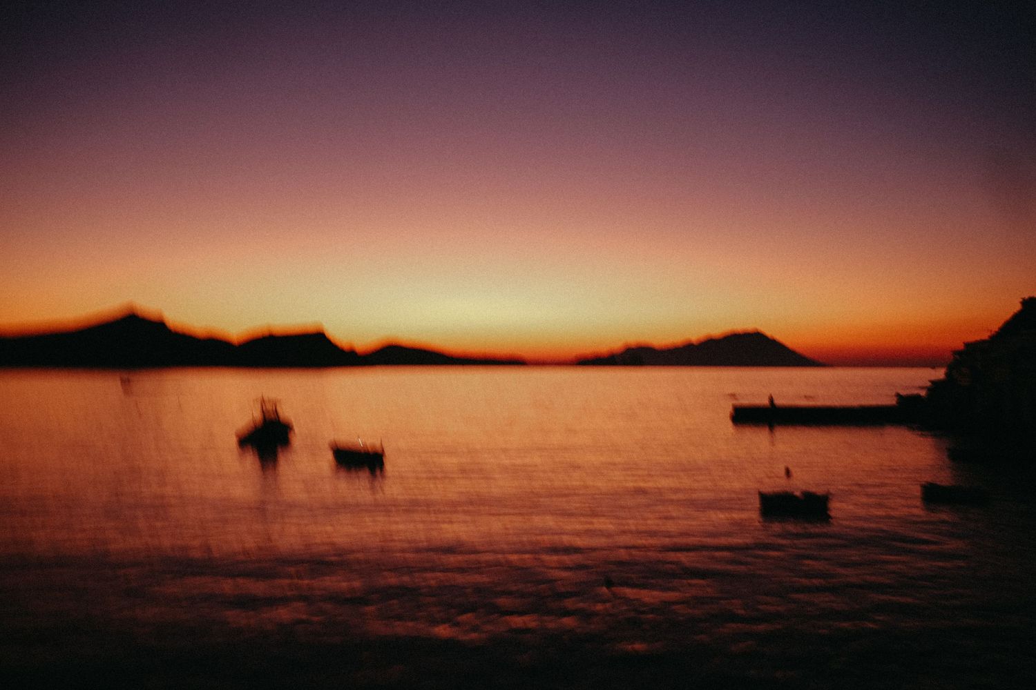 Silhouettes of boats at sunset with mountains in the background creating a peaceful seascape.