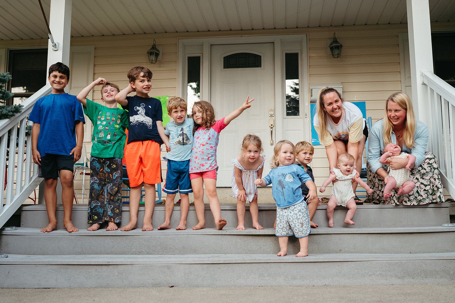 A lively group poses on a white porch during a casual summer gathering.