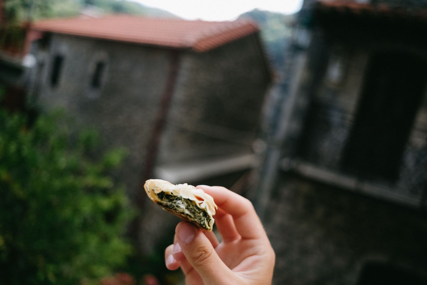 A hand holding a half-eaten sandwich against a rustic building backdrop.