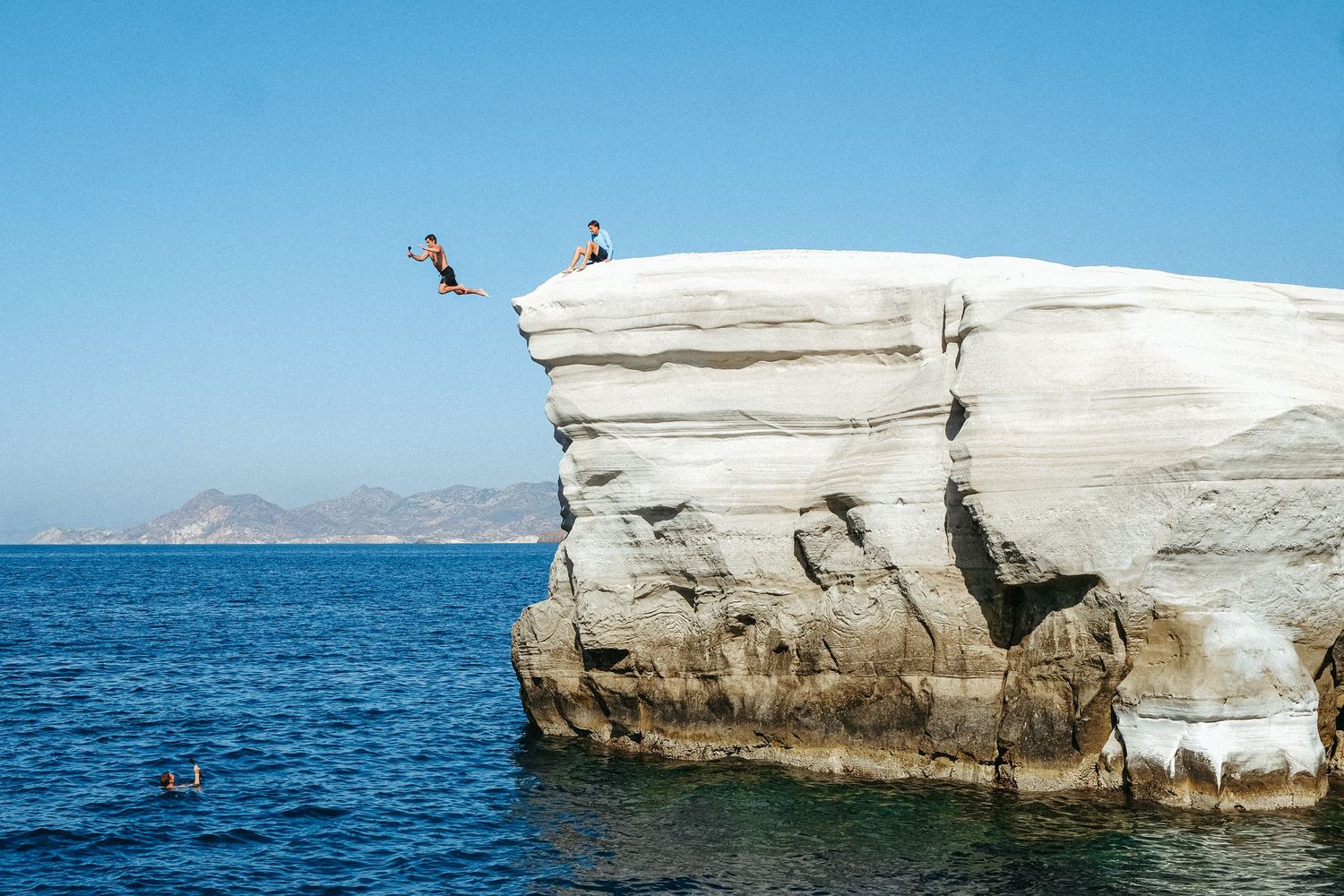 Someone diving off a white limestone cliff into blue ocean waters.