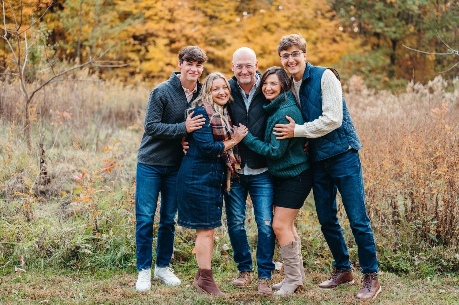 Group poses together outdoors during autumn with golden foliage in background.