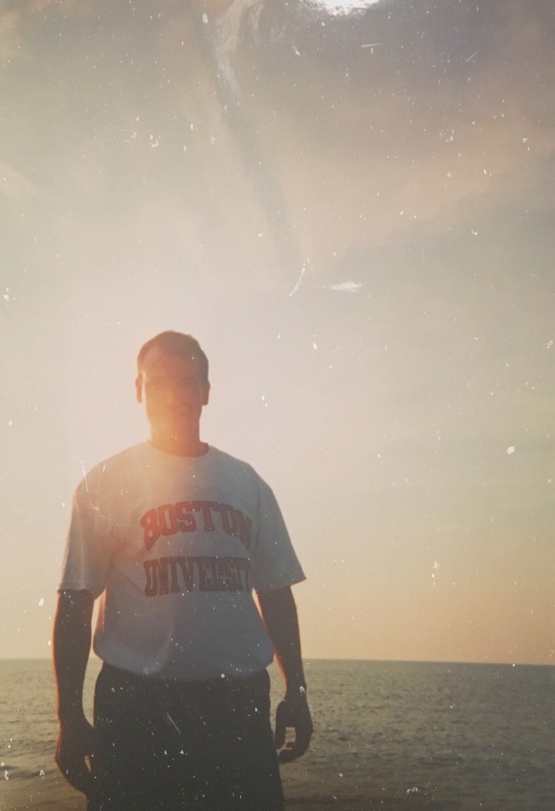 A silhouetted person wearing an Ohio State University shirt stands against a sunset sky over water.