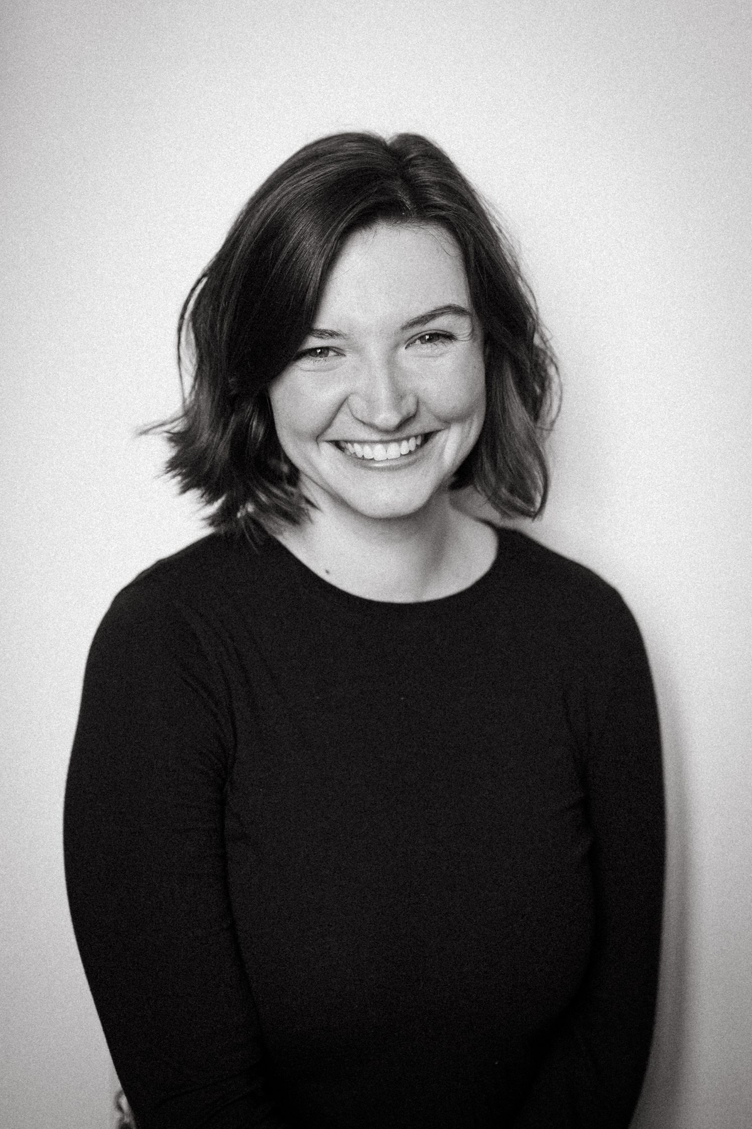 Black and white portrait of someone in dark sweater smiling at camera.