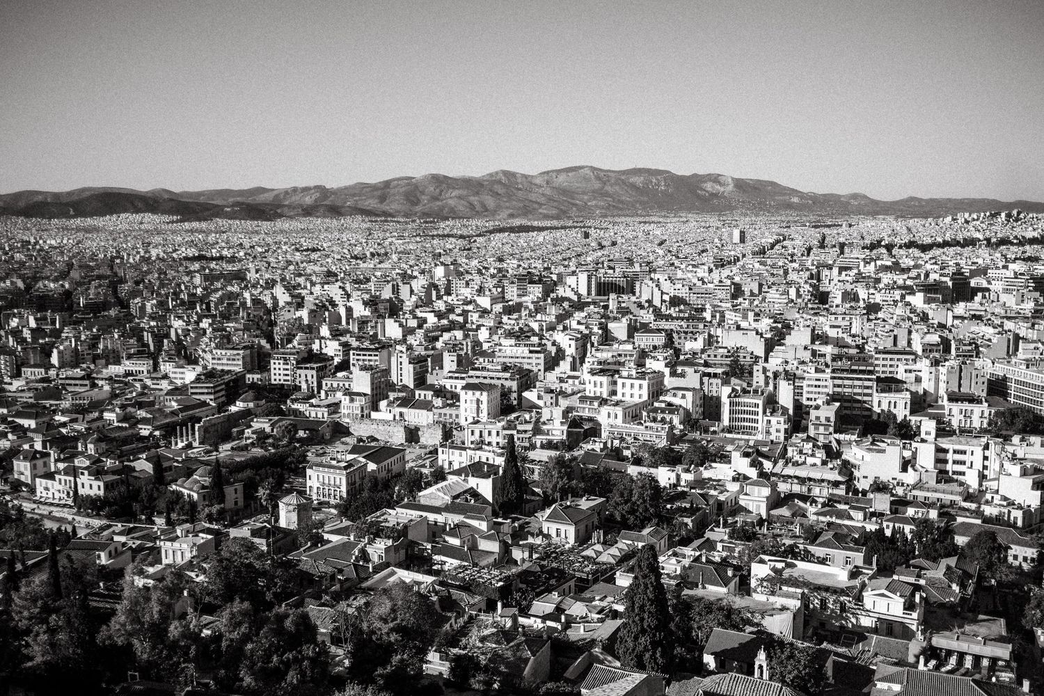Aerial black and white cityscape view of Athens sprawling towards distant mountains.