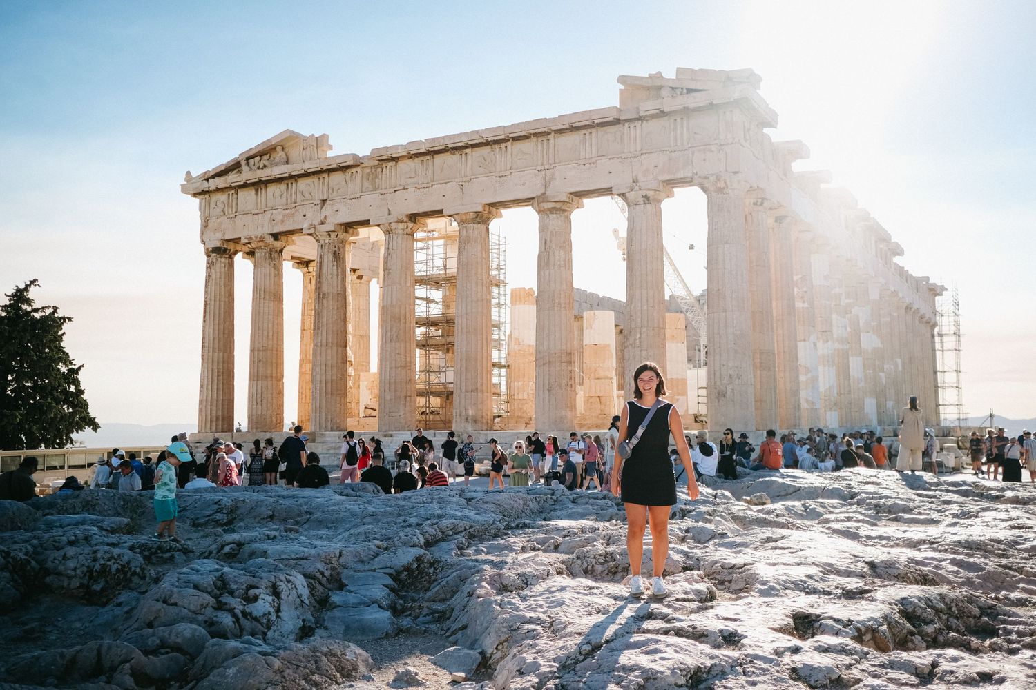 Tourists gather around the ancient Parthenon temple on the Acropolis in Athens during sunset.