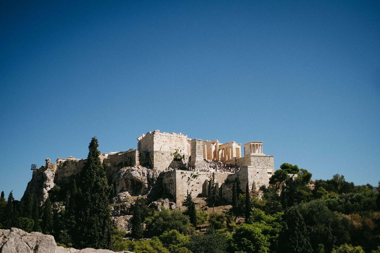 The Acropolis of Athens stands majestically on a hill against a bright blue sky.