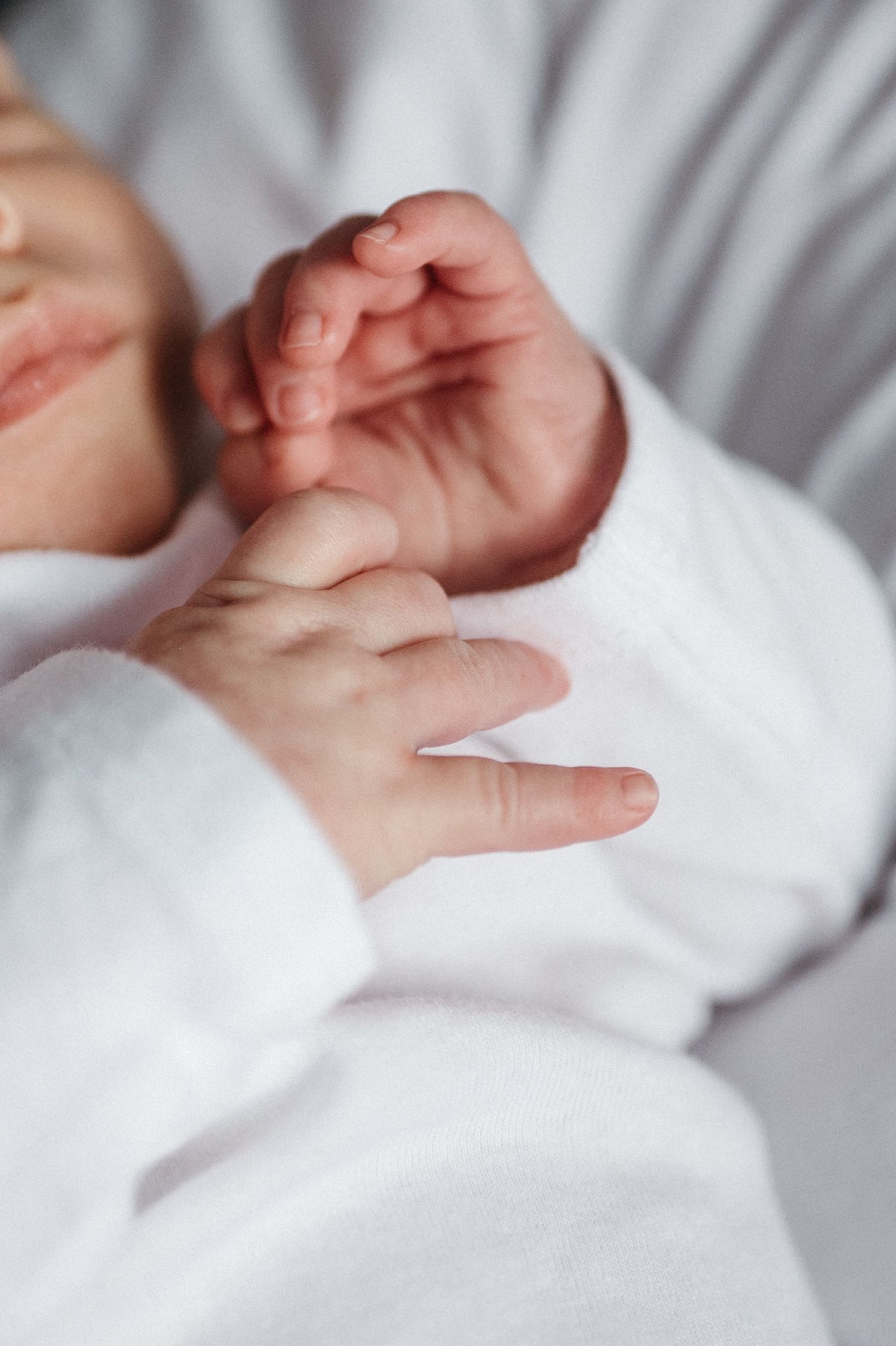 Close-up of baby's tiny hands in soft white fabric.